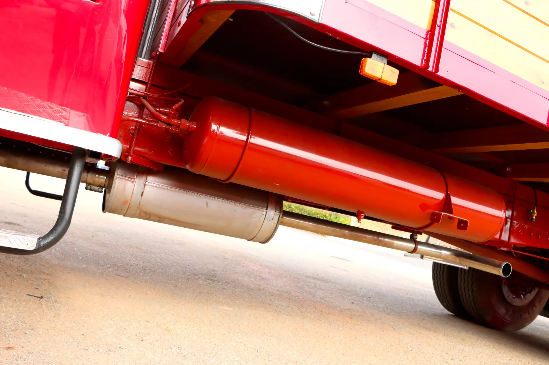 Primer plano de los bajos de un camión rojo que muestra un depósito de gasolina y un sistema de escape sobre una superficie pavimentada.