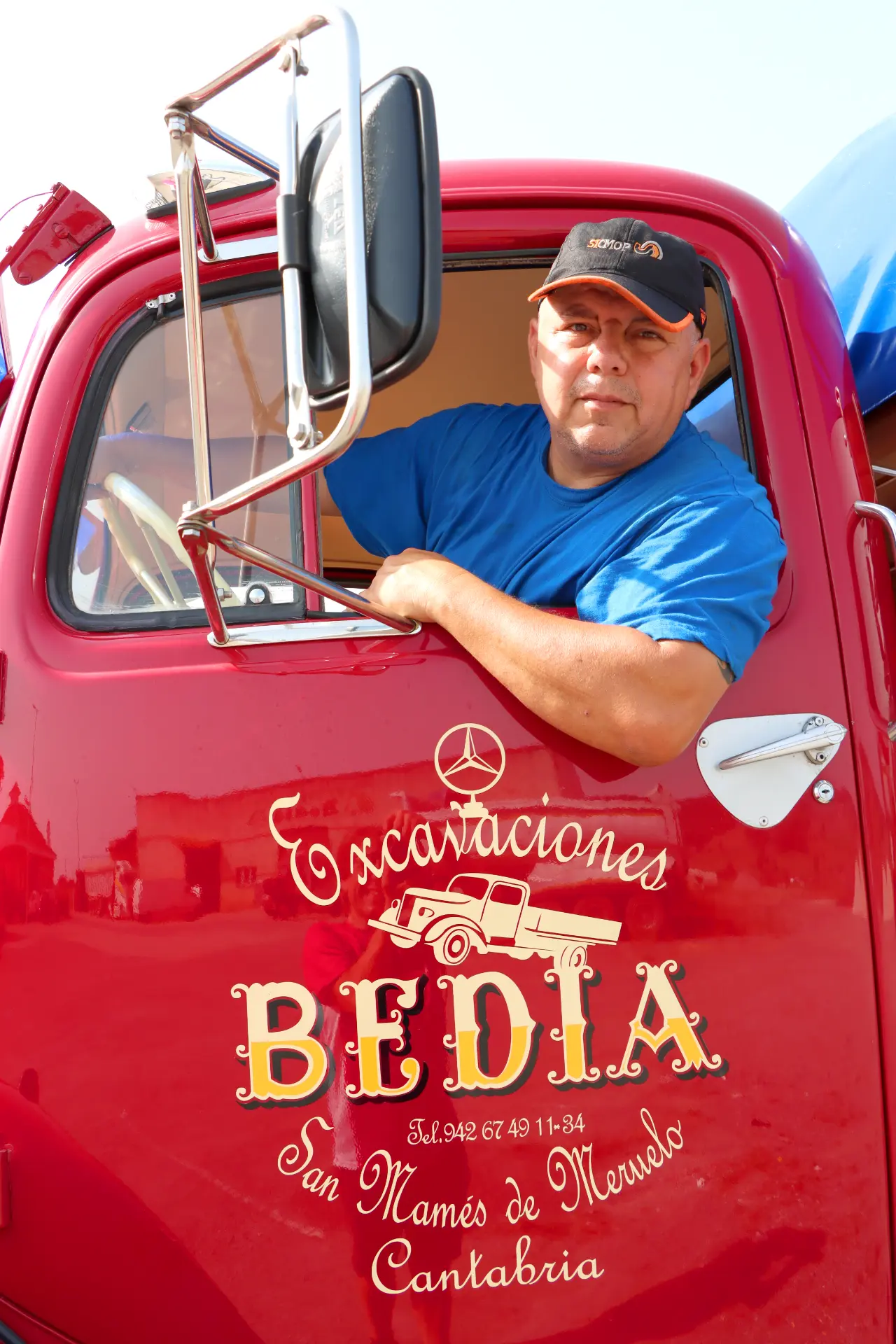 Hombre con camisa azul y gorra sentado en un camión rojo con "Excavaciones Bedia" escrito en la puerta.