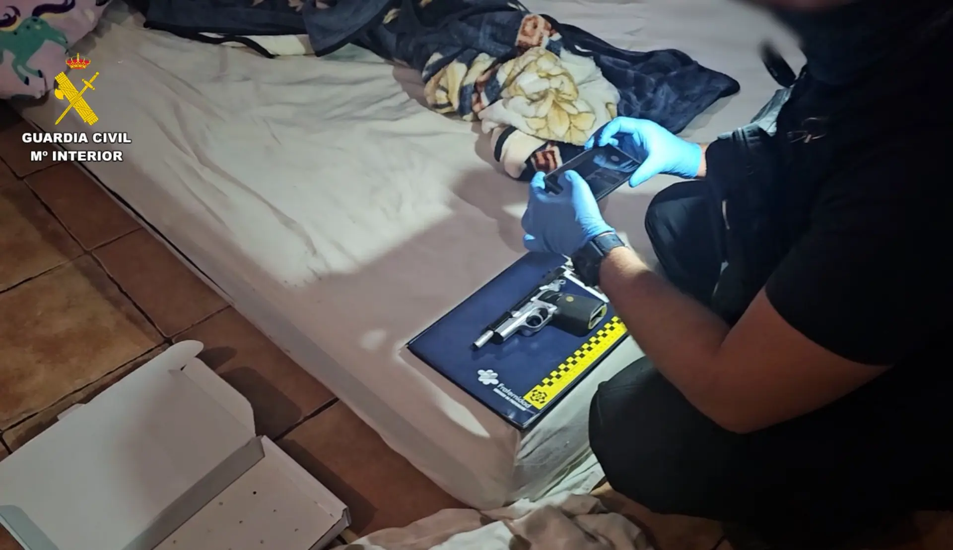 Un agente de policía fotografía un revólver sobre una cama durante una investigación sobre un asalto a un camionero, posiblemente relacionado con un clan familiar en La Mojonera.
