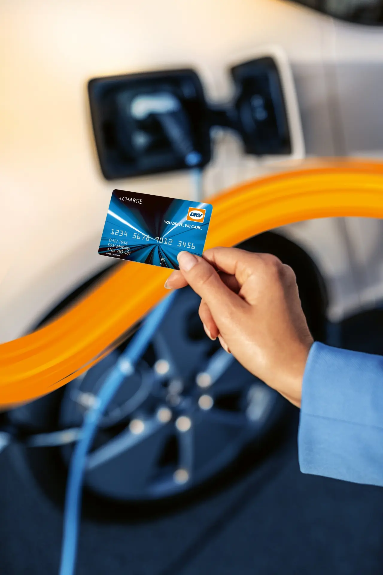 Una mano sostiene una tarjeta de combustible cerca de un coche eléctrico enchufado a una estación de carga con un swoosh naranja superpuesto, ilustrando el proceso de borrador automático.