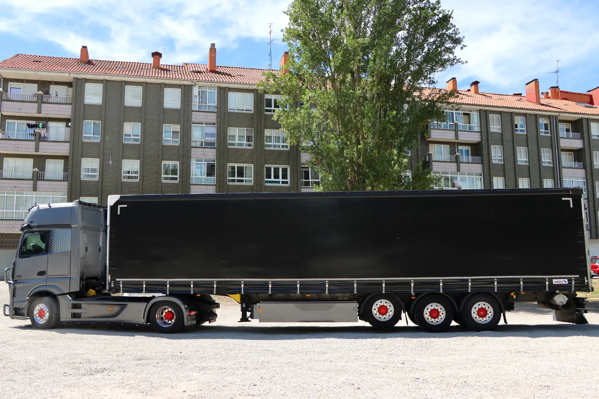 Un semirremolque negro con un largo remolque, rotulado "Borrador automático", está aparcado delante de un edificio de apartamentos.
