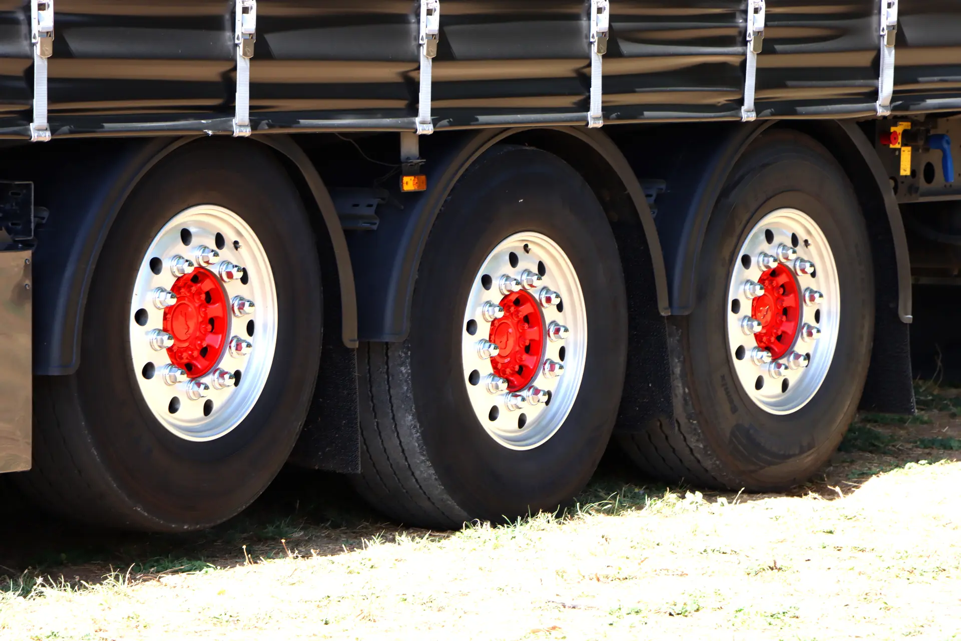 Primer plano de tres grandes ruedas de camión con llantas brillantes y cubos de rueda rojos, aparcadas sobre hierba: perfectas para mostrar la precisión de un borrador automático en el detallado de vehículos.