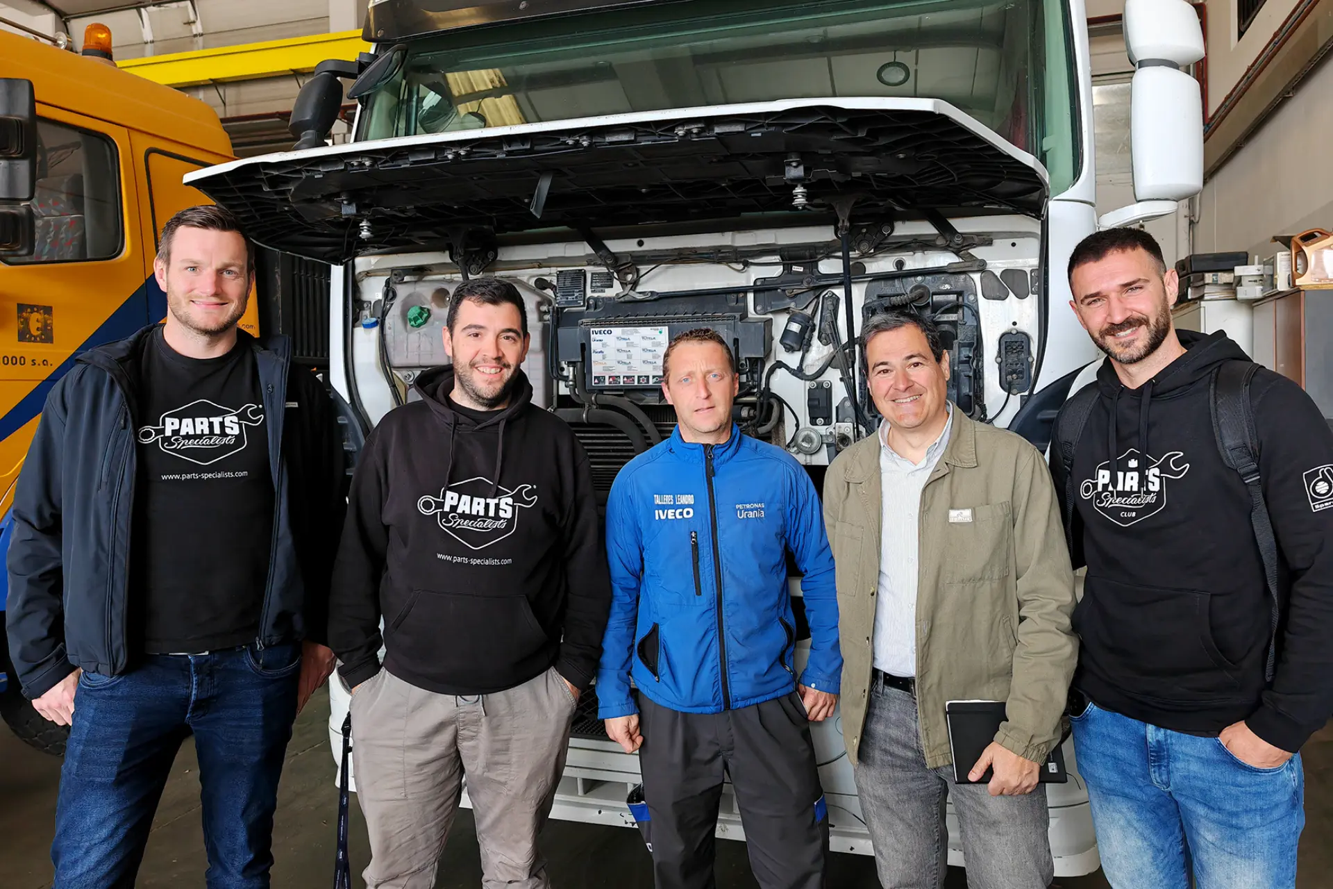Cinco hombres de pie delante de un camión con el capó abierto, posando y sonriendo para la foto en un taller de Diesel Technic.