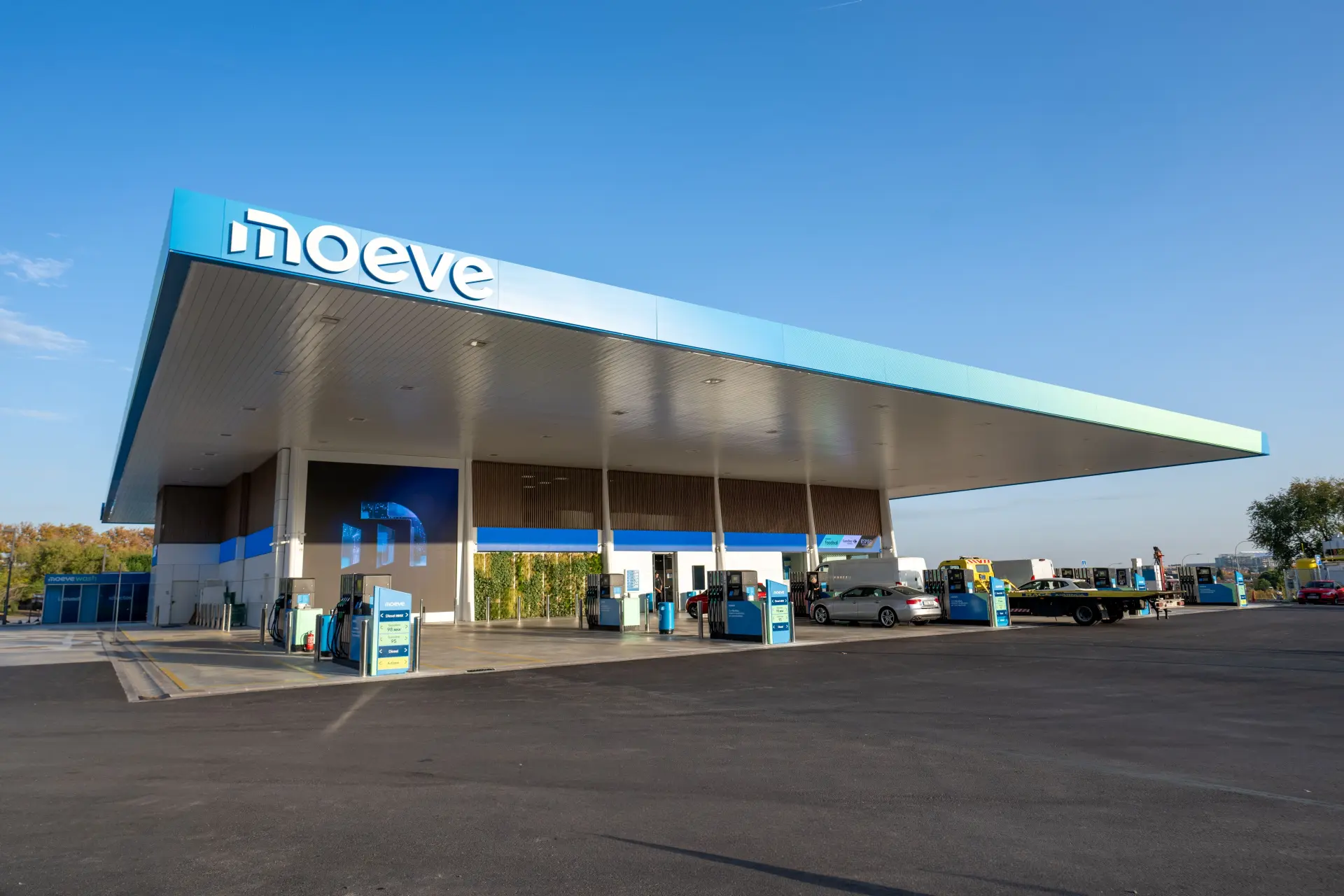 Moderna gasolinera con rótulos azules de Moeve bajo un cielo despejado, varios vehículos repostando: una de las muchas estaciones transformadas que hay ahora en España y Portugal.