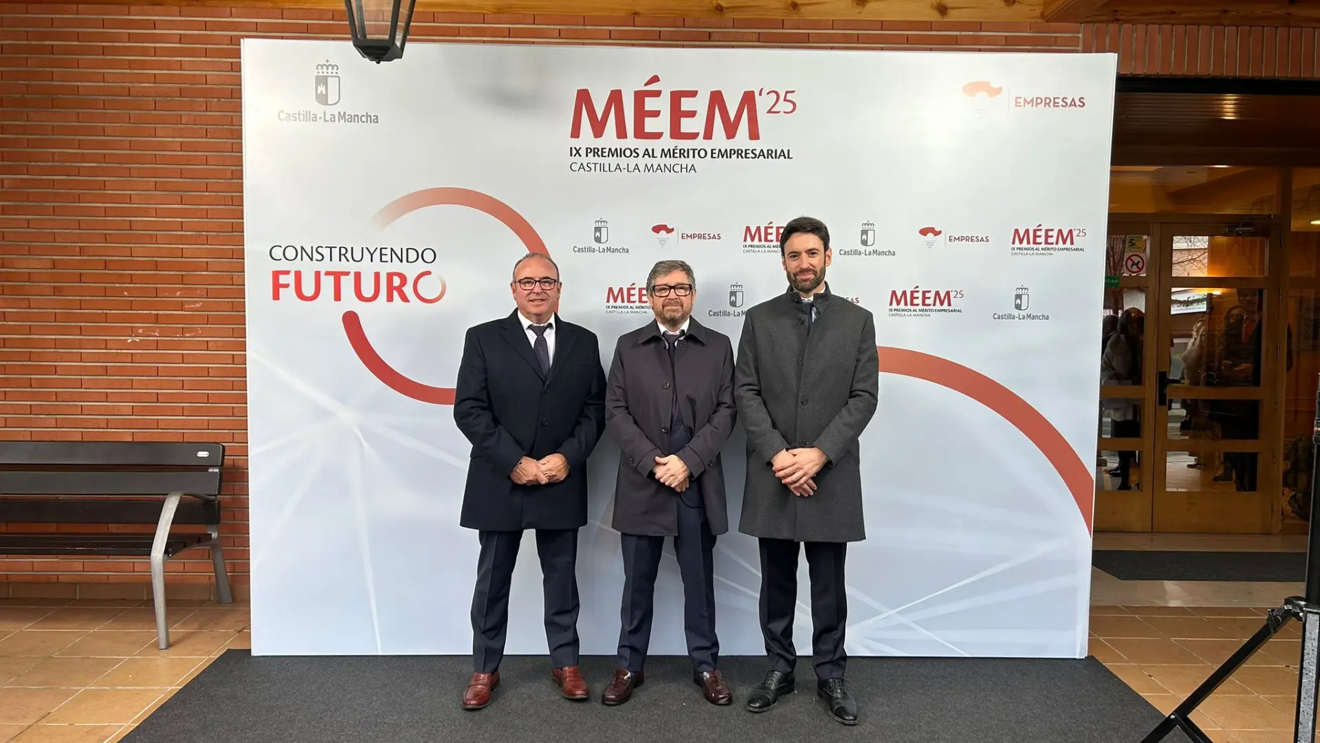 Tres hombres trajeados de pie delante de un telón de fondo de un acto de entrega de premios empresariales con "MÉEM'25", logotipos de Farcinox y la marca Premios al Mérito Empresarial de Castilla-La Mancha.