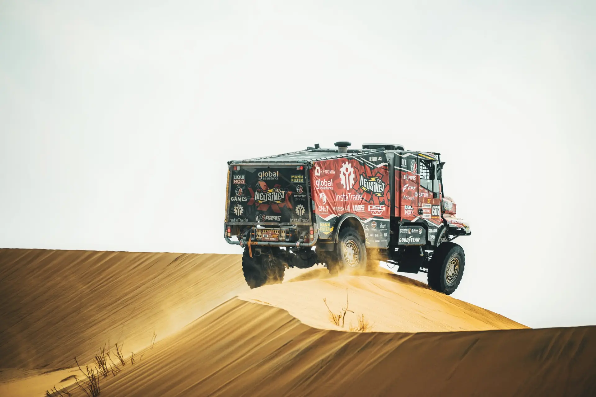 Un camión de rally del equipo De Rooy levanta arena al pasar por una duna en el paisaje desértico del Dakar durante una carrera.