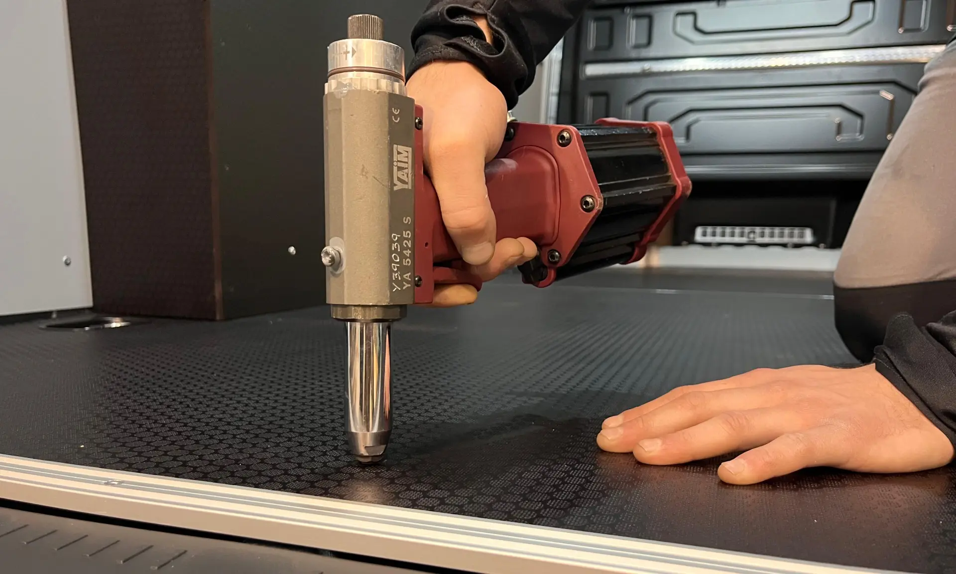 Una persona utiliza una herramienta eléctrica con borrador automático para fijar o sujetar un panel de superficie, con las manos claramente visibles.