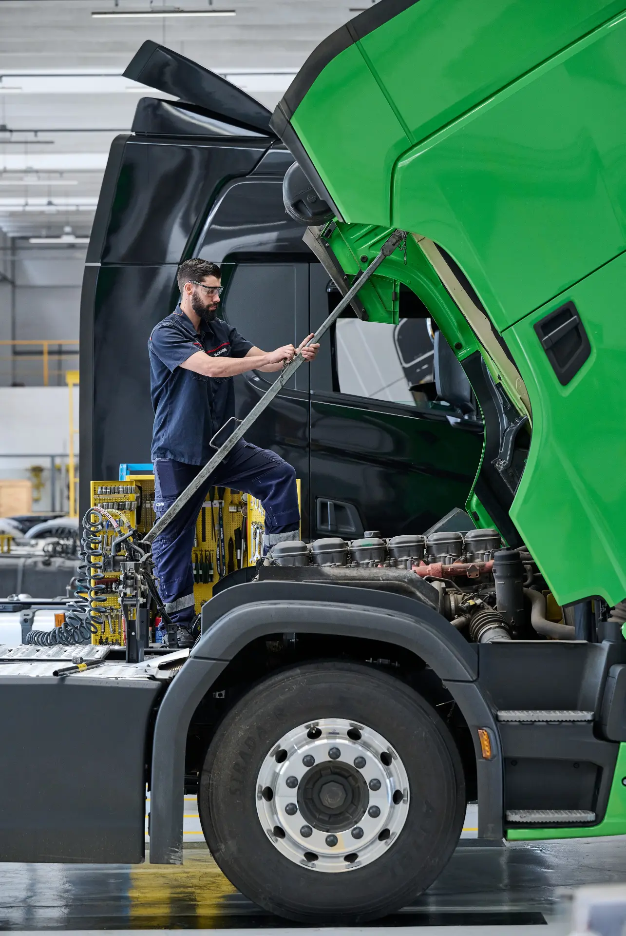 Un mecánico inspecciona el motor de un semirremolque verde en un garaje industrial.