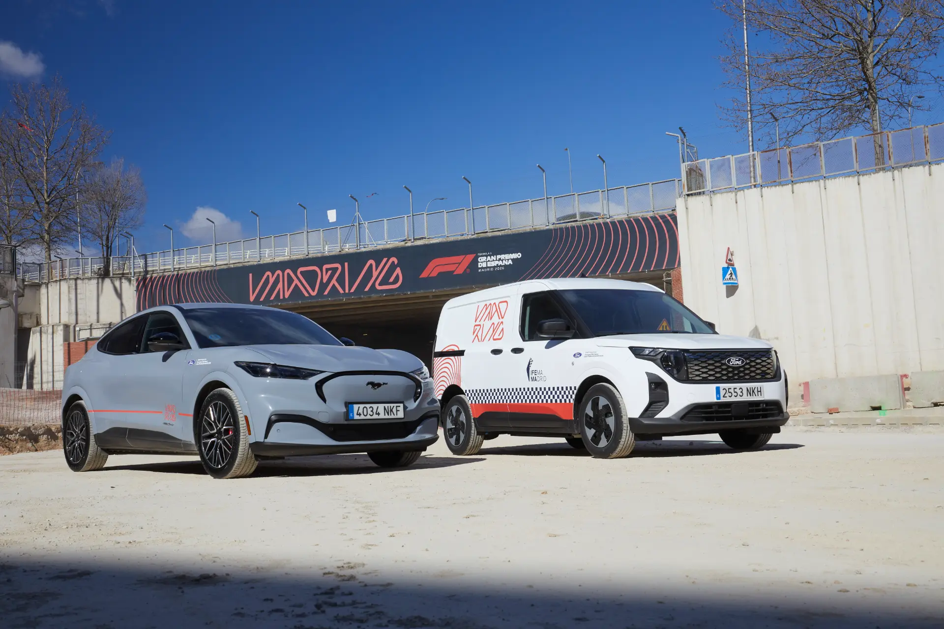 Dos vehículos eléctricos aparcados frente a la entrada de un circuito de carreras con el letrero "Madrid" de F1 en lo alto, captados como parte de una secuencia de Borrador automático.