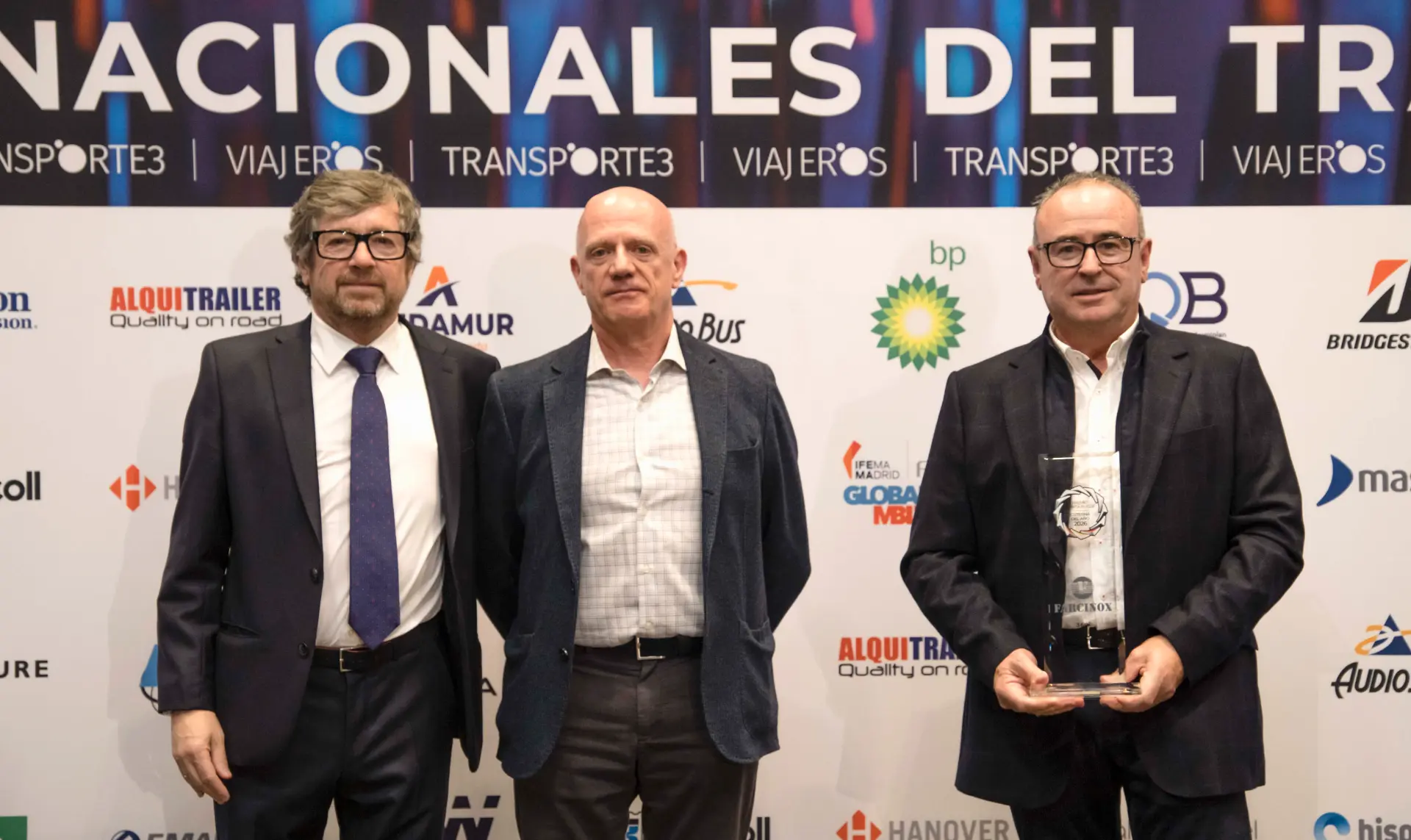 Tres hombres trajeados de pie juntos, uno de ellos sosteniendo un premio de cristal para Cisterna del Año 2026, delante de un telón de fondo del evento Farcinox 360º.