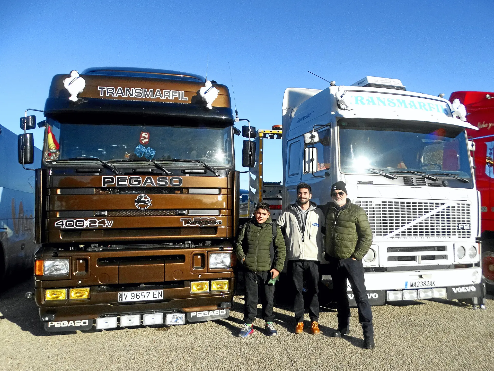 Tres hombres sonríen entre un Pegaso marrón y un Volvo blanco -camiones clásicos- bajo el cielo azul de la Ribera del Duero.