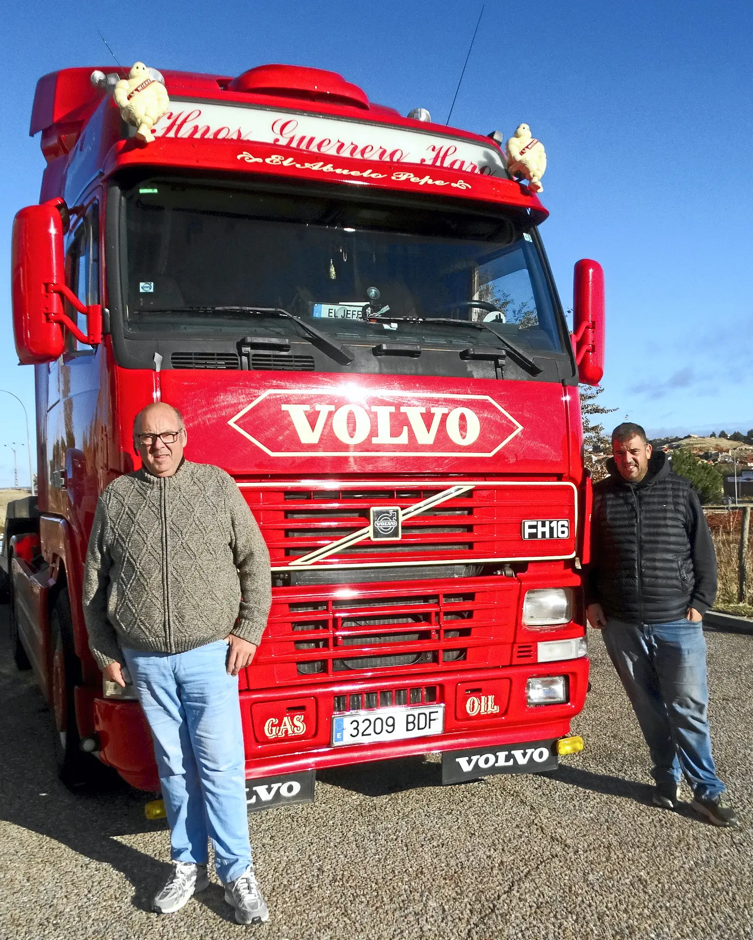 Dos hombres frente a un camión Volvo FH16 rojo, uno de los más destacados entre los camiones clásicos, aparcado en un día soleado.