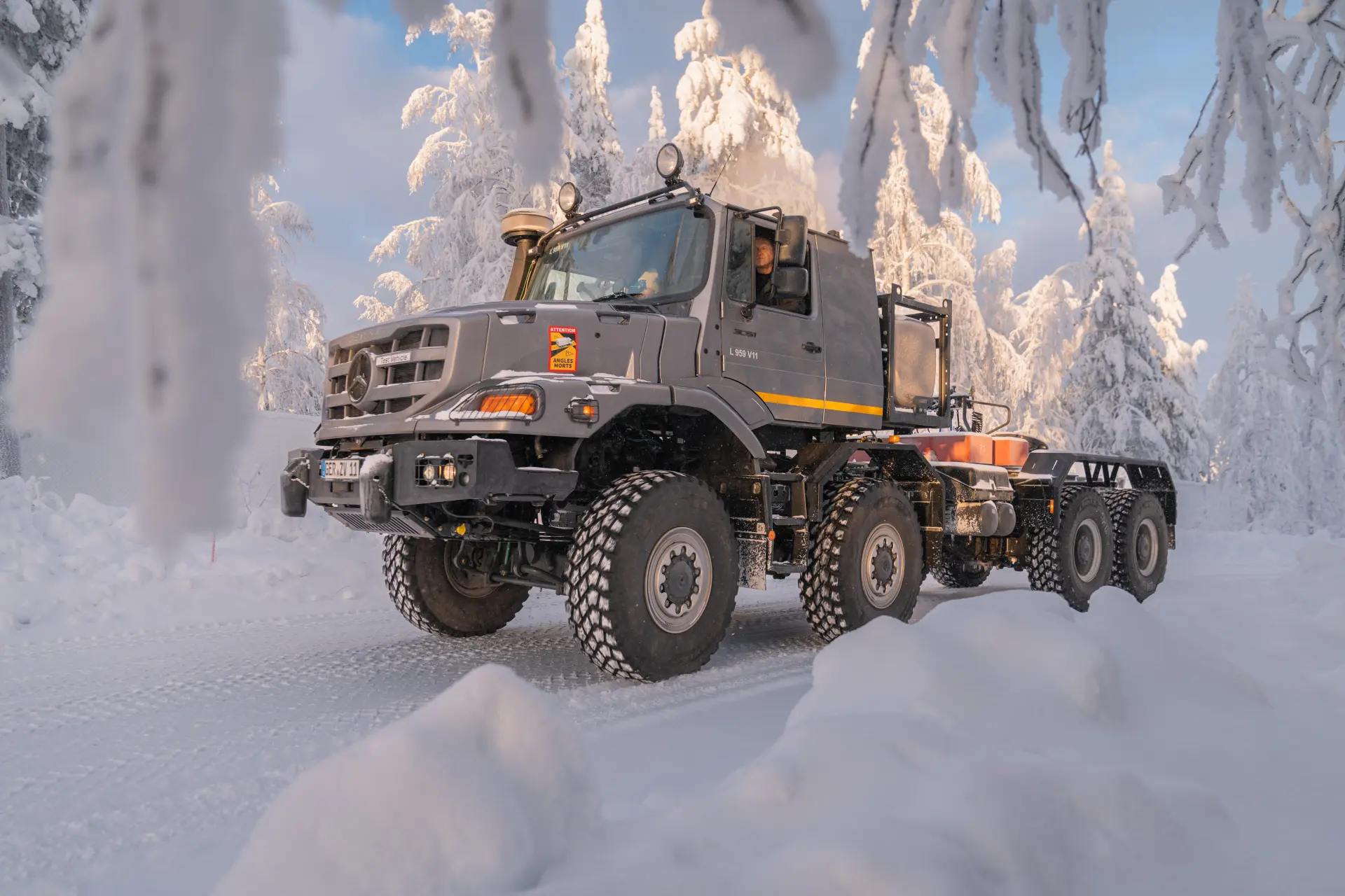 Un Mercedes-Benz Zetros realiza pruebas árticas mientras atraviesa un bosque nevado en Finlandia, con árboles cargados de nieve al fondo.