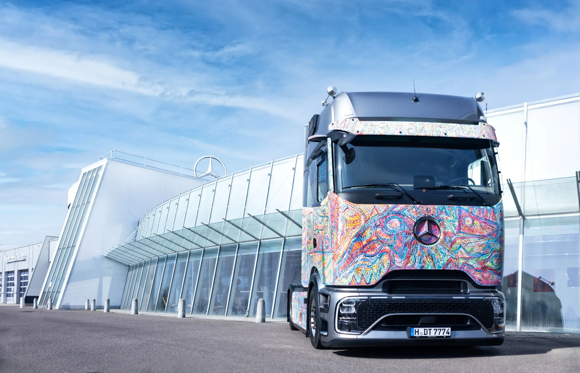 Un colorido y estampado Mercedes-Benz Actros L ProCabin camión decorado gira Alemania está aparcado frente a un moderno edificio de cristal, mostrando el vibrante estilo de los camiones de larga distancia.