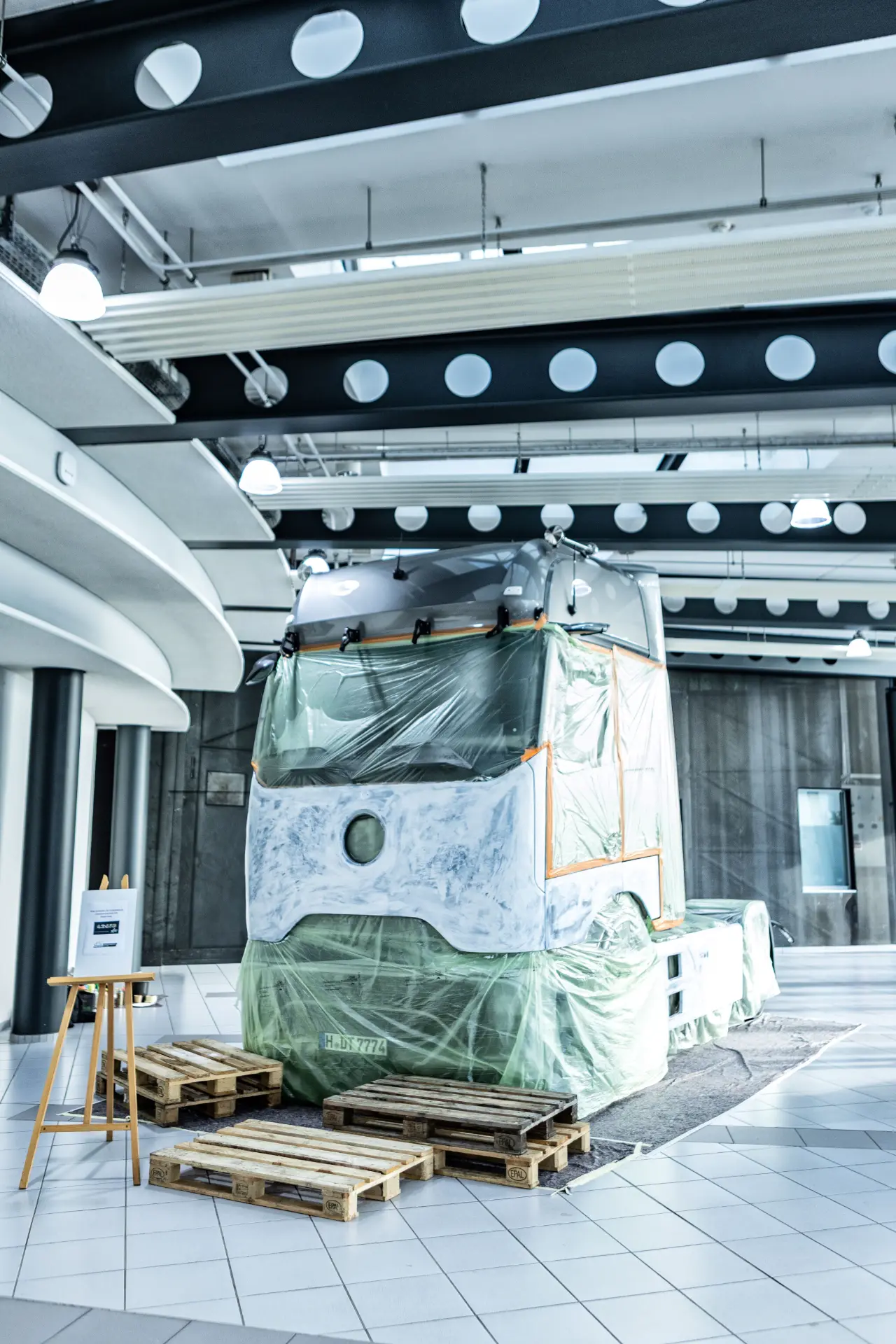 Un tranvía parcialmente cubierto se exhibe en el interior junto a palés y elegantes elementos de diseño, evocando el espíritu innovador del Actros edición art truck.