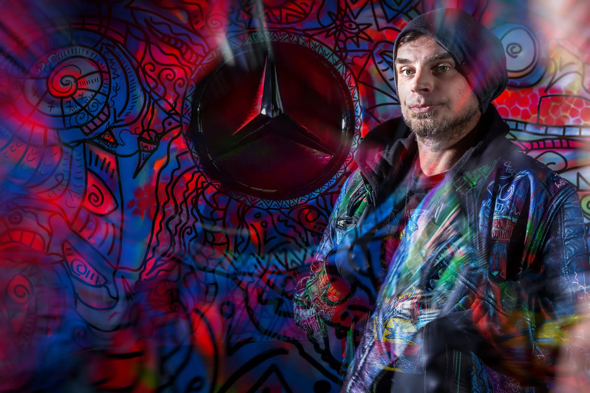 Un hombre con una chaqueta con capucha junto a coloridos grafitis, luces de neón y el logotipo de Mercedes-Benz, evocando el vibrante espíritu de los Actros edición art truck que se ven en los camiones de larga distancia en Alemania.