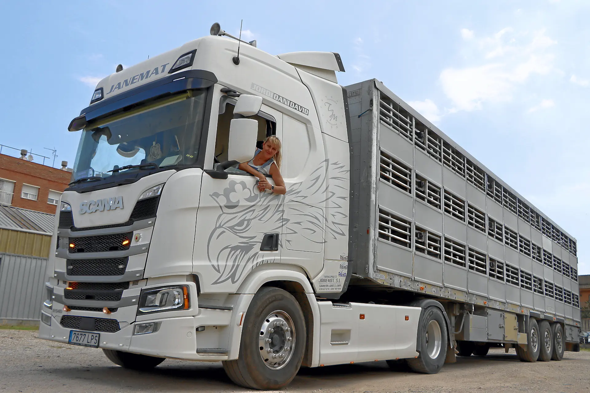 Janet Torres, encarnando el espíritu de "Soy Camionera", se asoma a la ventanilla de un gran camión blanco de transporte de ganado aparcado al aire libre.