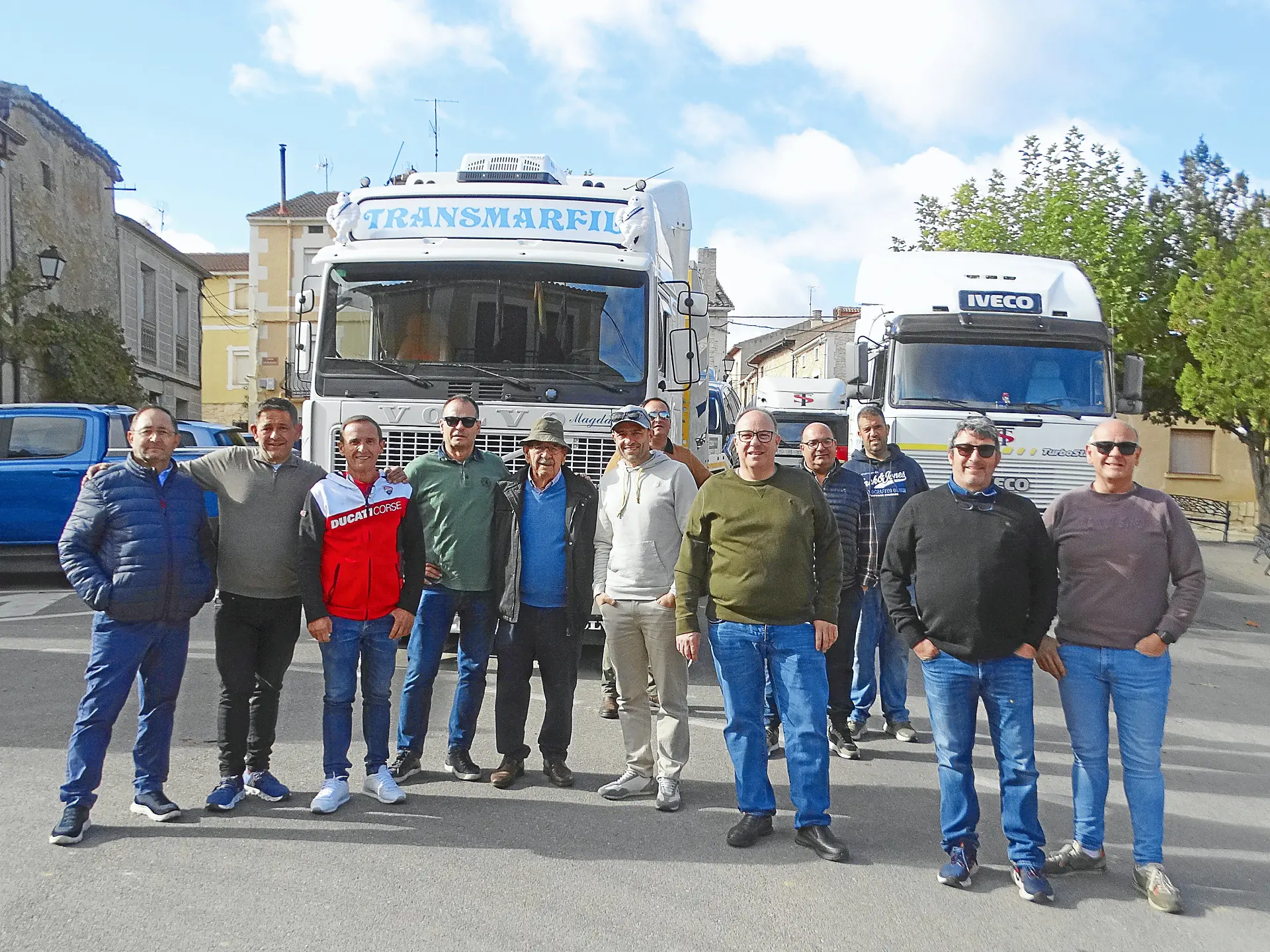 Doce hombres posan delante de dos grandes camiones aparcados en una calle soleada para una foto de grupo como parte del equipo Borrador automático.