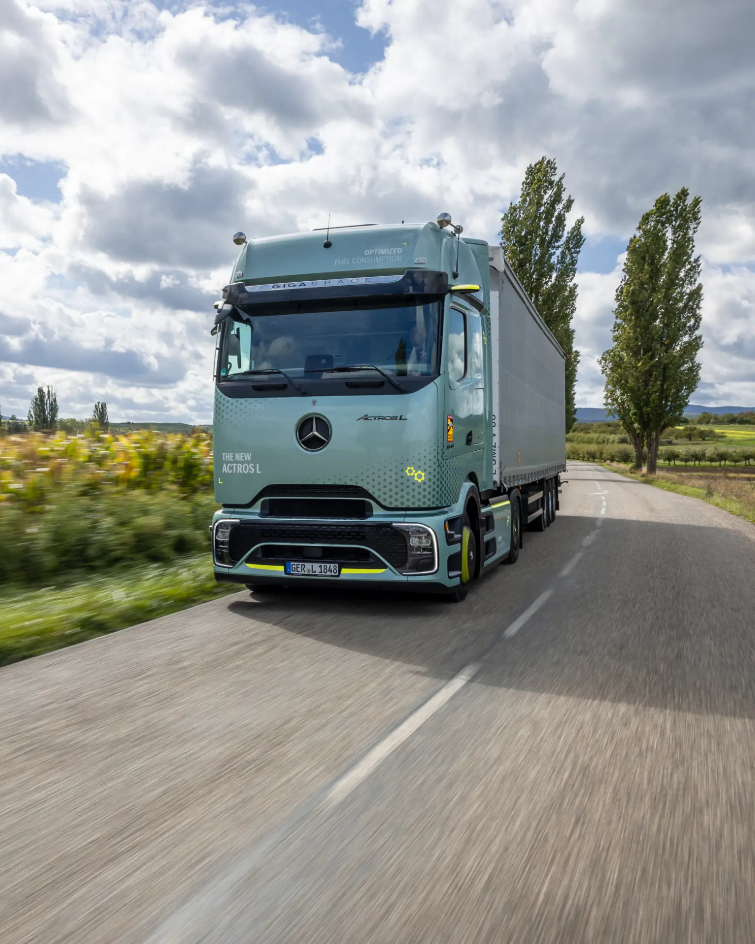 Un camión Mercedes-Benz eActros 600 circula por una carretera rural bordeada de árboles bajo un cielo nublado, mostrando la impresionante autonomía de los camiones eléctricos para el transporte de larga distancia.