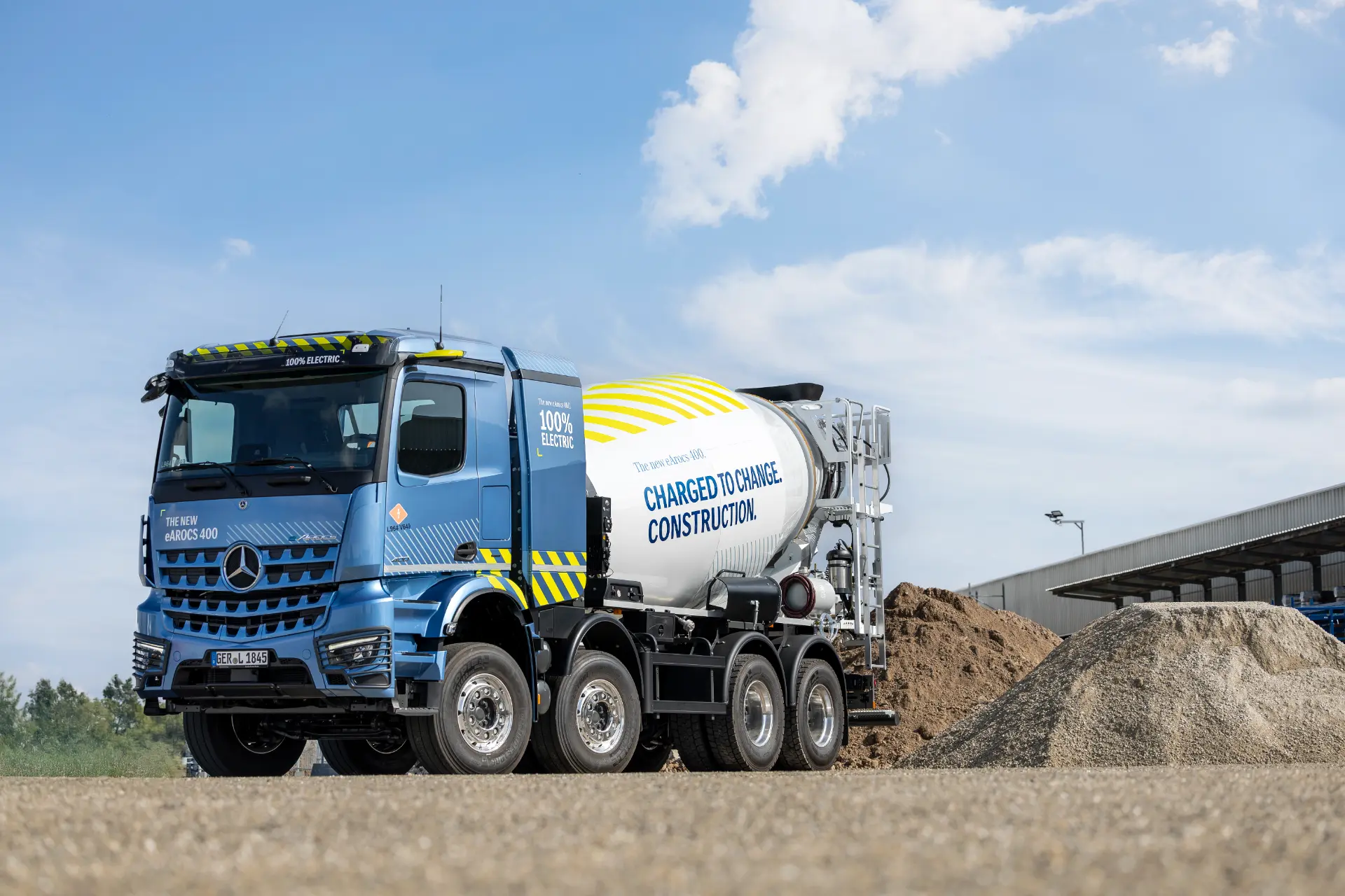 Un camión cementero eléctrico eActros 400 azul con cabina Mercedes ProCabin está aparcado en una obra junto a un montón de tierra bajo un cielo despejado.