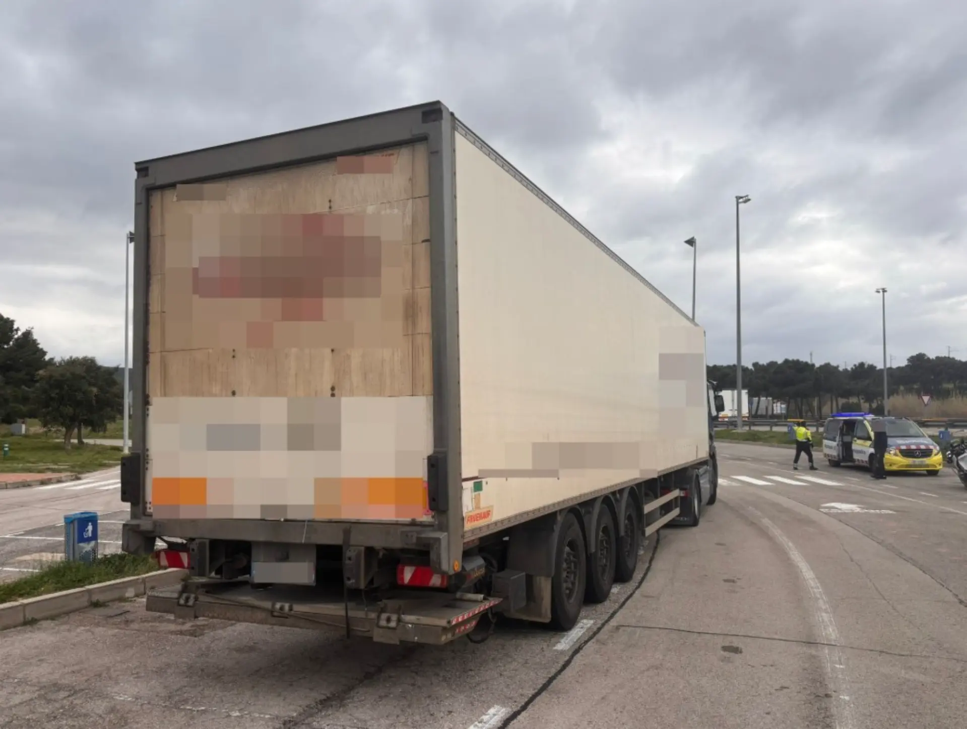 Un semirremolque blanco con el remolque cerrado está aparcado en una carretera cerca de agentes de policía y vehículos en La Jonquera después de que infracciones de tacógrafo provocaran una multa récord.