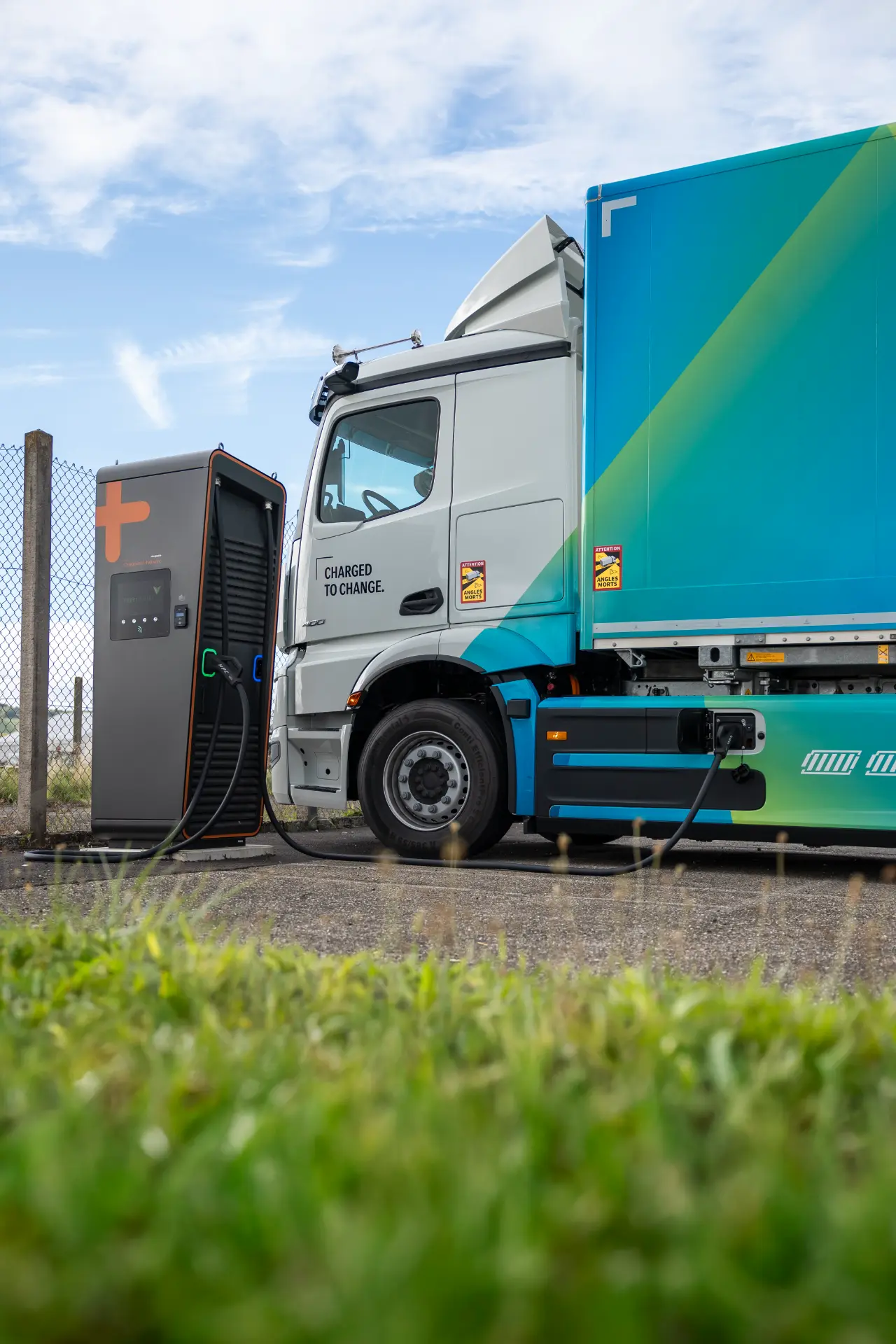 Un camión eléctrico eActros 600 se carga en una estación de carretera en un día despejado, mostrando la innovadora tecnología de la serie ProCabin de Mercedes.