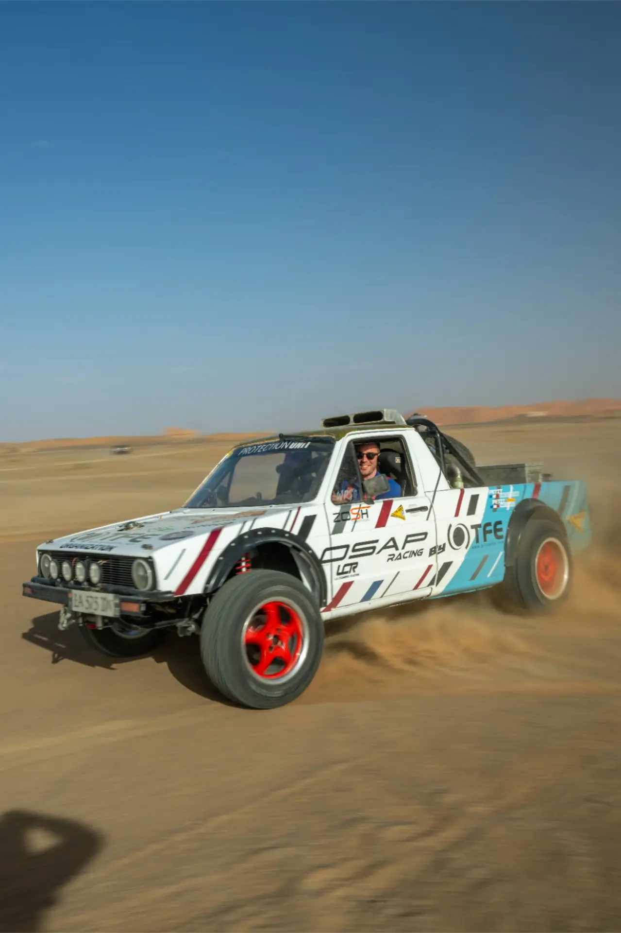 Un Volkswagen todoterreno de raid blanco con ruedas rojas levanta polvo mientras corre por las pistas de Marruecos durante la 12 edición Golf Challenge Algeciras.