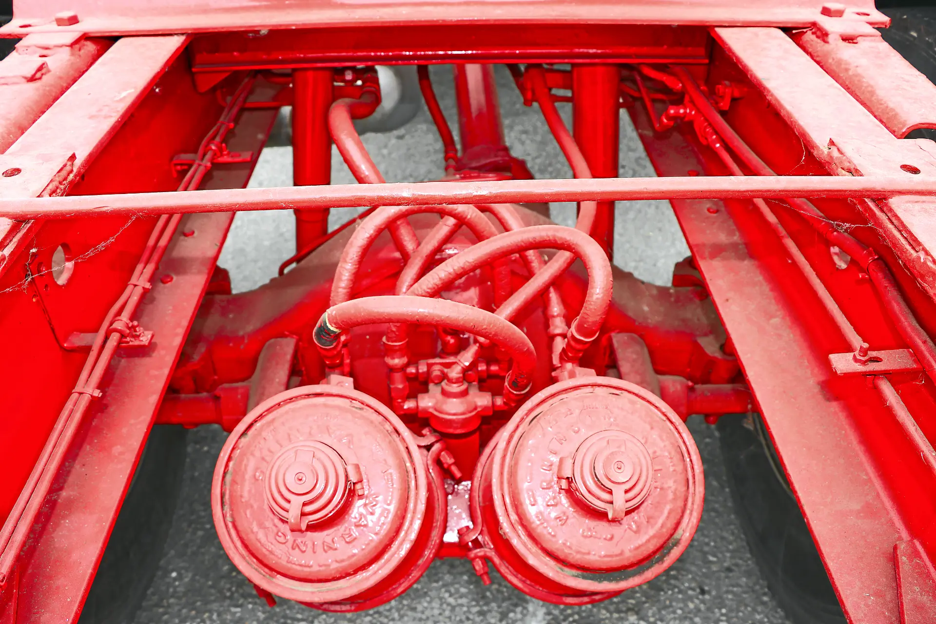Chasis de camión pintado en rojo de Cresmotrans, con suspensión visible, sistema de frenos de aire y componentes mecánicos, ideal para camiones clásicos o proyectos Náuticos & Especiales.