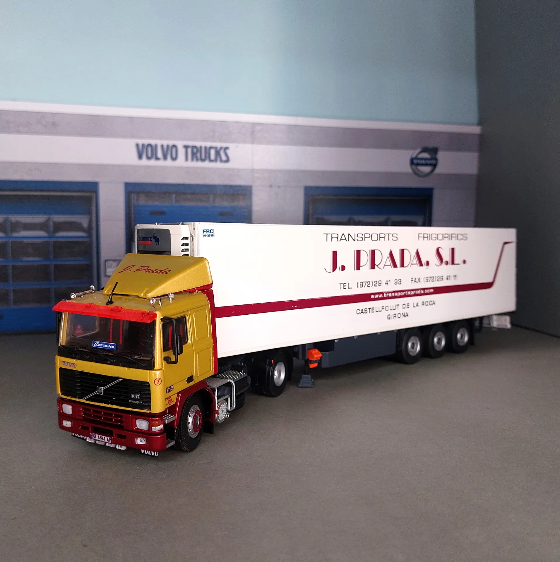 Un camión Volvo amarillo con un remolque blanco está aparcado delante de un edificio de Volvo Trucks, listo para siembre y recolecta mercancías, tal y como imaginó Juan Carlos Carrasco.