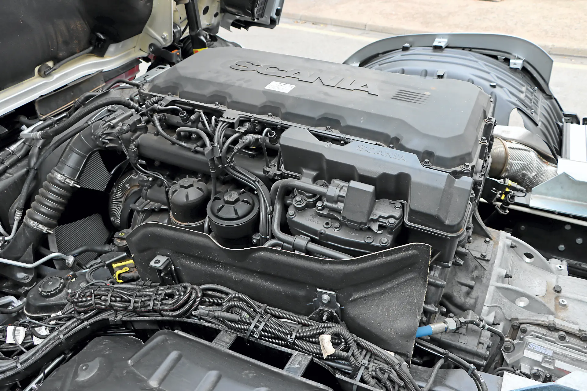 Primer plano del motor de un camión Scania con varios cables, tuberías y componentes visibles, destacando la integración del sistema de borrador automático.