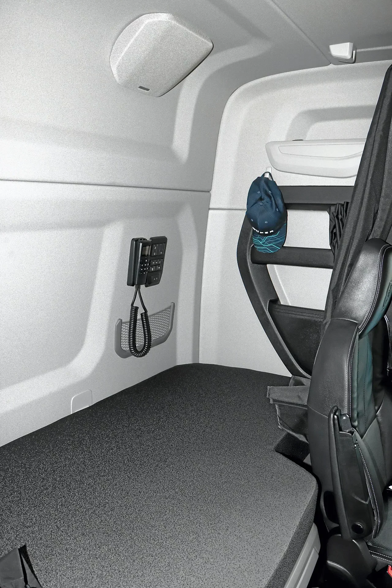 Interior de una cabina dormitorio de camión con borrador automático, radio CB, un cómodo asiento y un sombrero apoyado en la litera superior plegada.