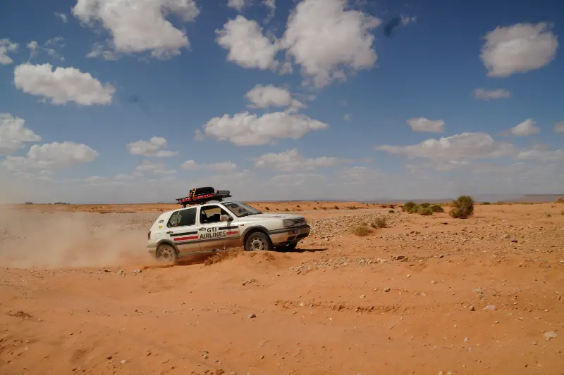Un todoterreno blanco atraviesa un paisaje desértico arenoso bajo un cielo parcialmente nublado, levantando polvo durante el emocionante VW Challenge 2026.