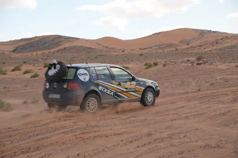 Un coche de rally con el número 42 corre por un arenoso paisaje desértico, levantando polvo tras de sí en el emocionante VW Challenge 2026, encarnando el verdadero espíritu de aventura 4x4.