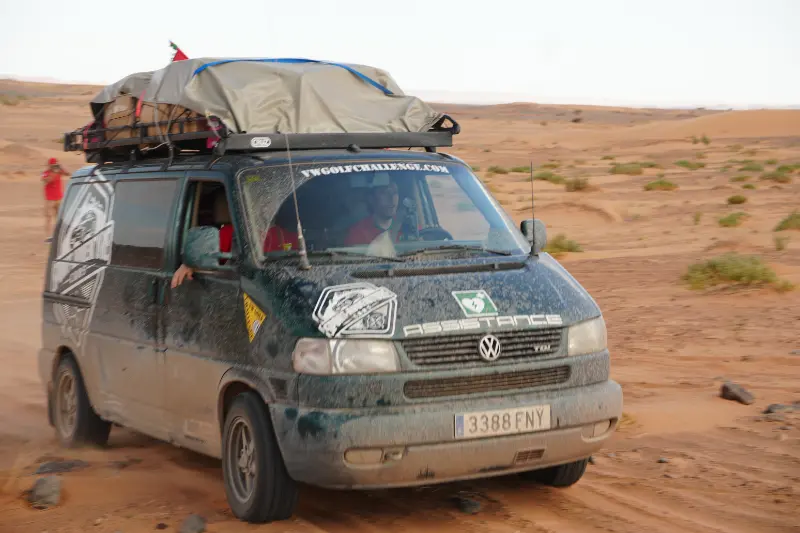 Una polvorienta furgoneta con equipaje en el techo atraviesa el paisaje desértico de Marruecos, con dos personas en su interior embarcadas en una aventura 4x4, listas para el VW Challenge 2026.