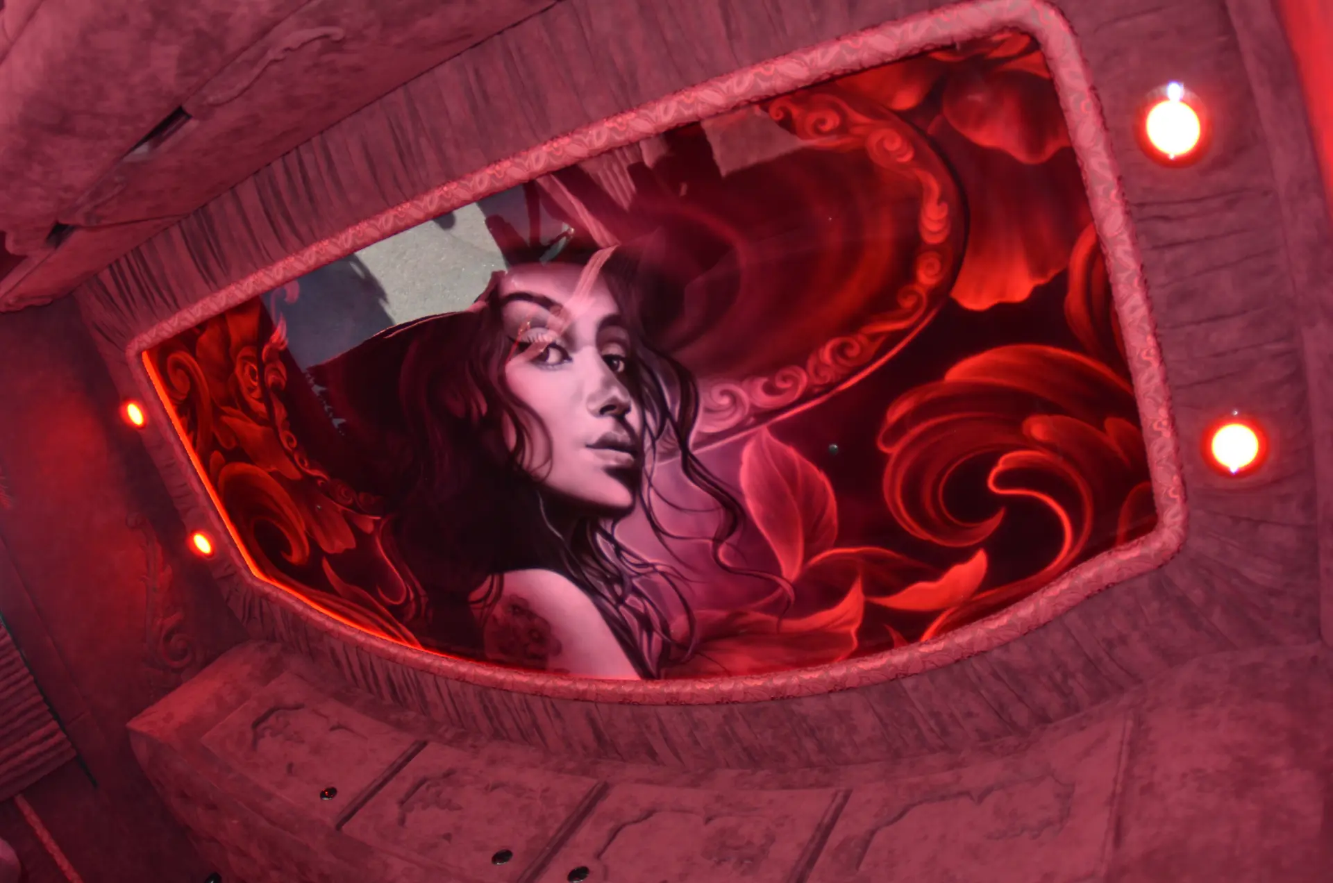Un mural de una mujer con cuernos en un escenario de fantasía rojo y lleno de pasión, rodeada de flores y motivos arremolinados: una obra de arte que recuerda la vibrante energía de Carmen y Sascha Heinrichs.