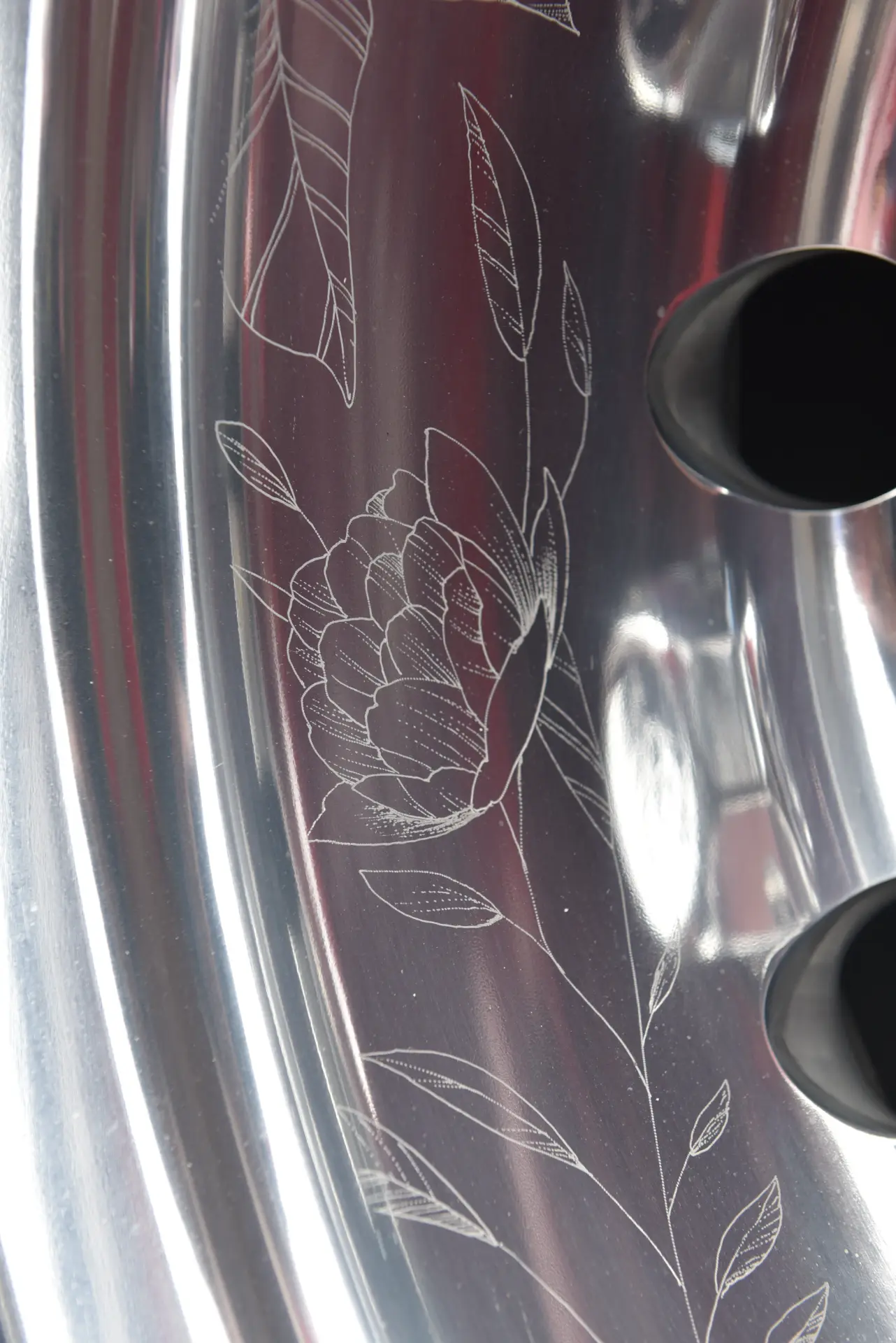 Primer plano de una llanta de coche de metal brillante con un diseño floral grabado, que refleja la pasión y la artesanía que recuerdan a Carmen y Sascha Heinrichs.