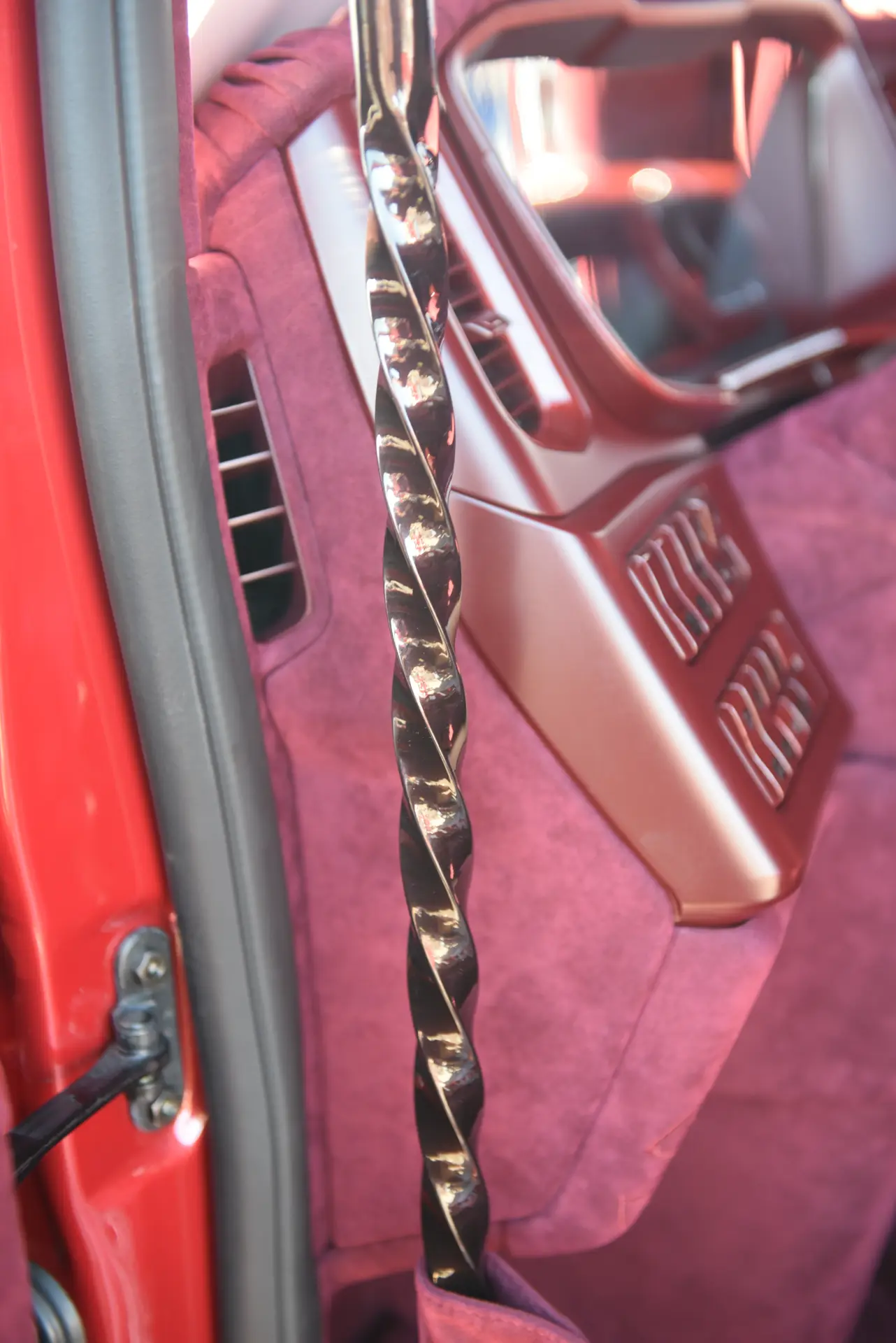 Primer plano del interior de un coche personalizado con tapicería de felpa morada y un asa de agarre brillante y retorcida, hecha con la pasión que define a Carmen y Sascha Heinrichs.