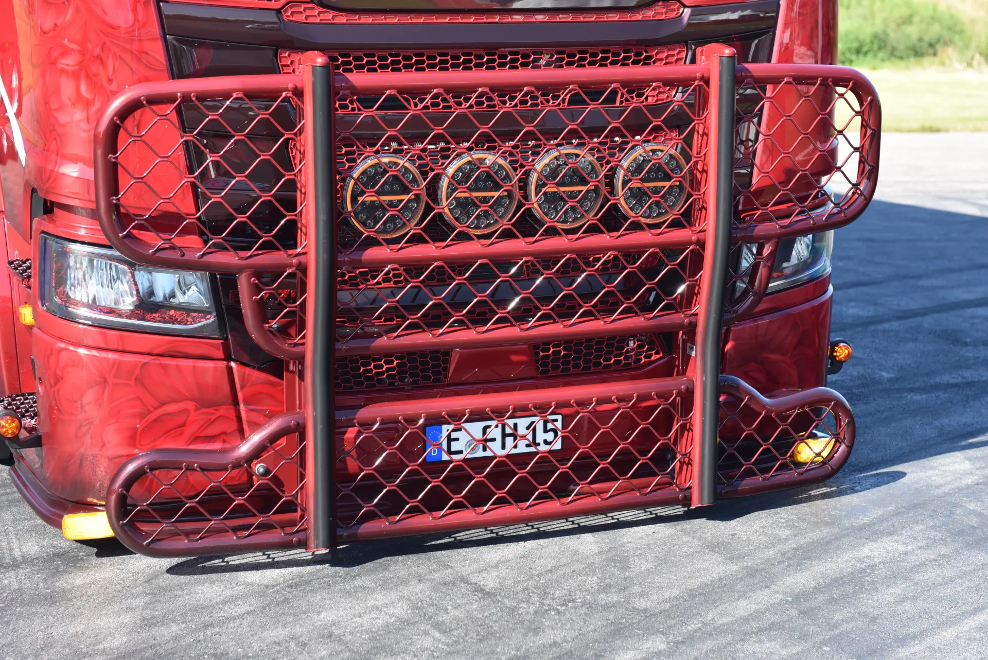 Primer plano de la parrilla delantera de un camión Scania R770 rojo con un protector metálico y una matrícula europea, que capta la pasión de Carmen y Sascha Heinrichs por los vehículos potentes.