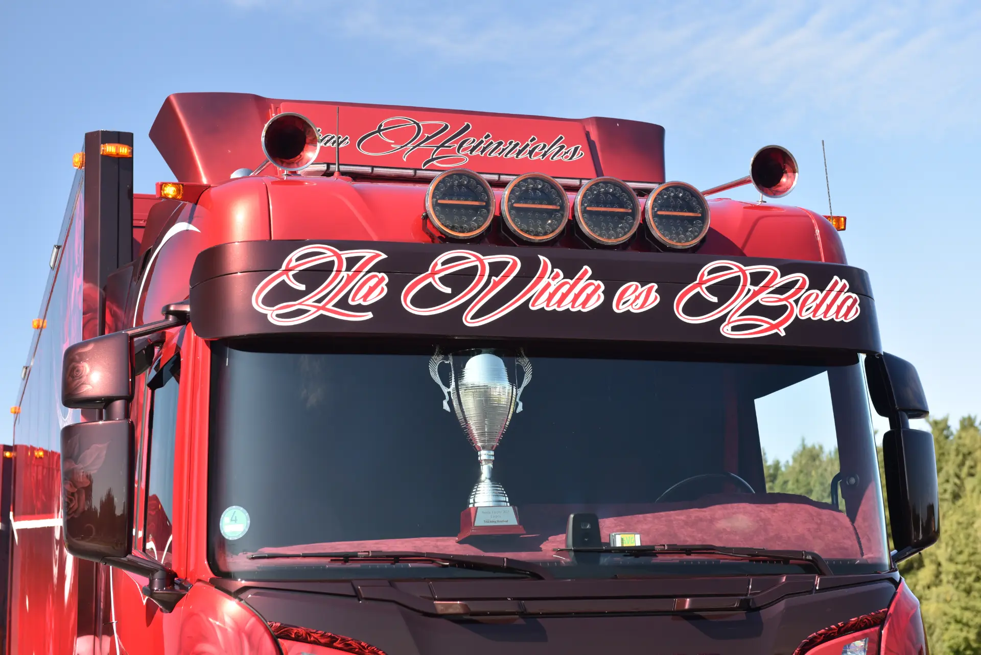 Camión Scania R770 rojo con "La Vida es Bella" en el parabrisas, un trofeo en el salpicadero: la pasión brilla en cada detalle del vehículo de Carmen y Sascha Heinrichs.