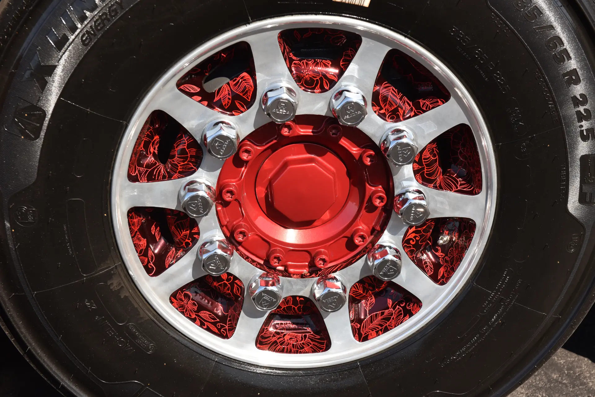 Primer plano de un neumático de camión Scania R770 con un brillante cubo de rueda decorativo cromado y rojo y tuercas de orejeta visibles, que refleja la pasión de Carmen y Sascha Heinrichs por el detalle excepcional.