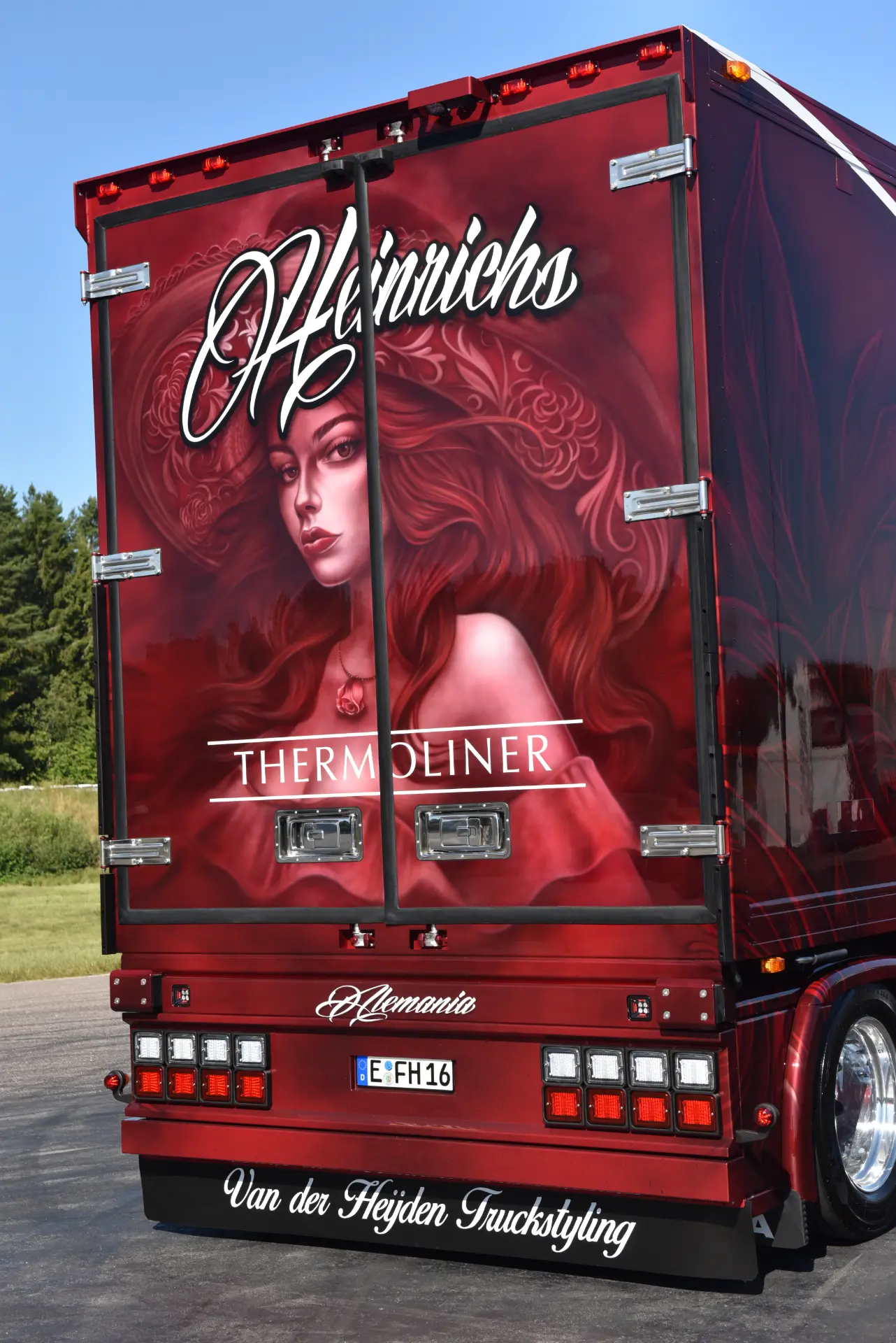 En la parte trasera de un camión Scania R770 rojo aparece la imagen de una mujer pelirroja con sombrero, junto a la palabra "Heinrichs".