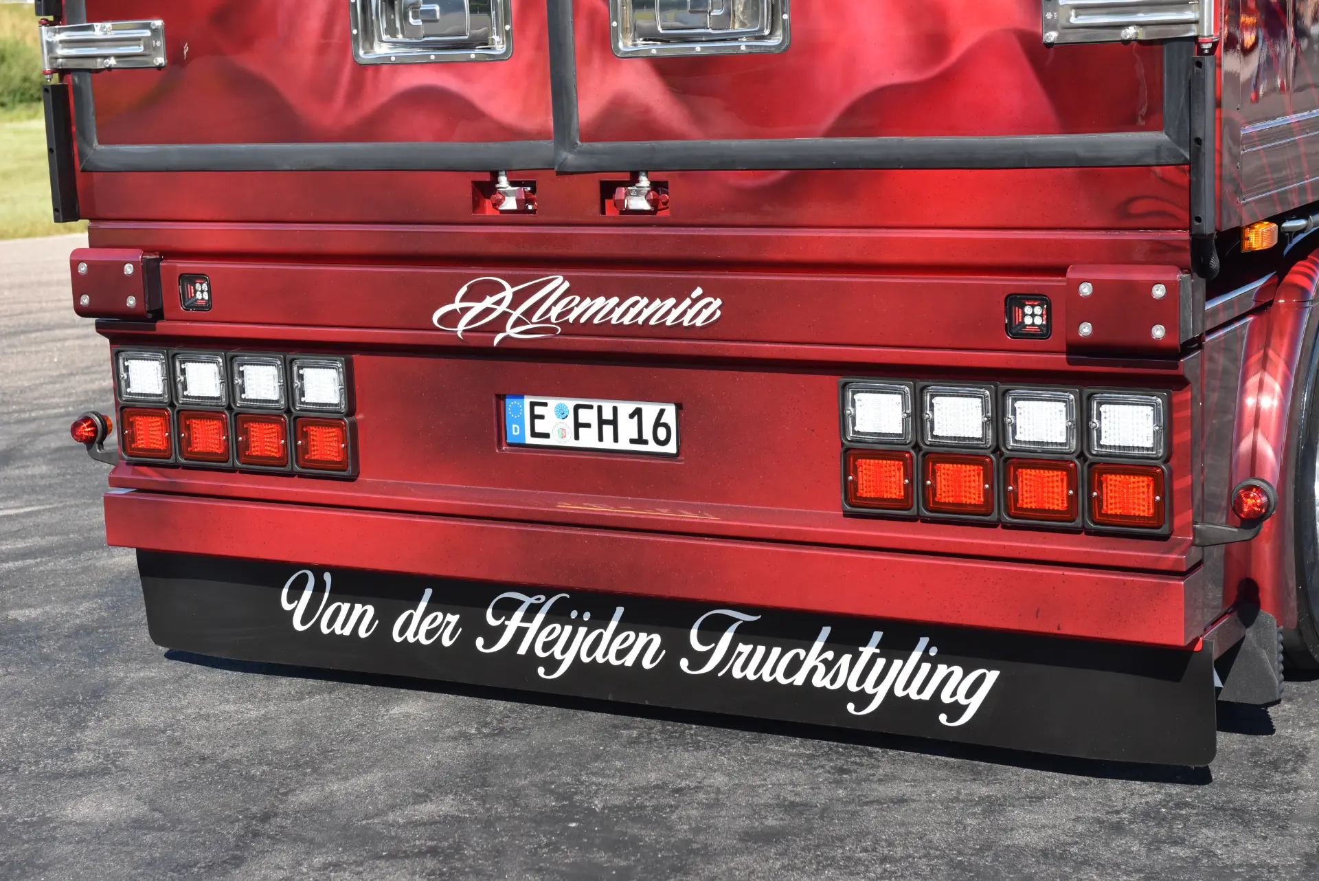 Parte trasera de un camión Scania R770 rojo con los rótulos "Alemania" y "Van der Heijden Truckstyling", luces LED y los nombres de Carmen Heinrichs y Sascha Heinrichs en la parte trasera.
