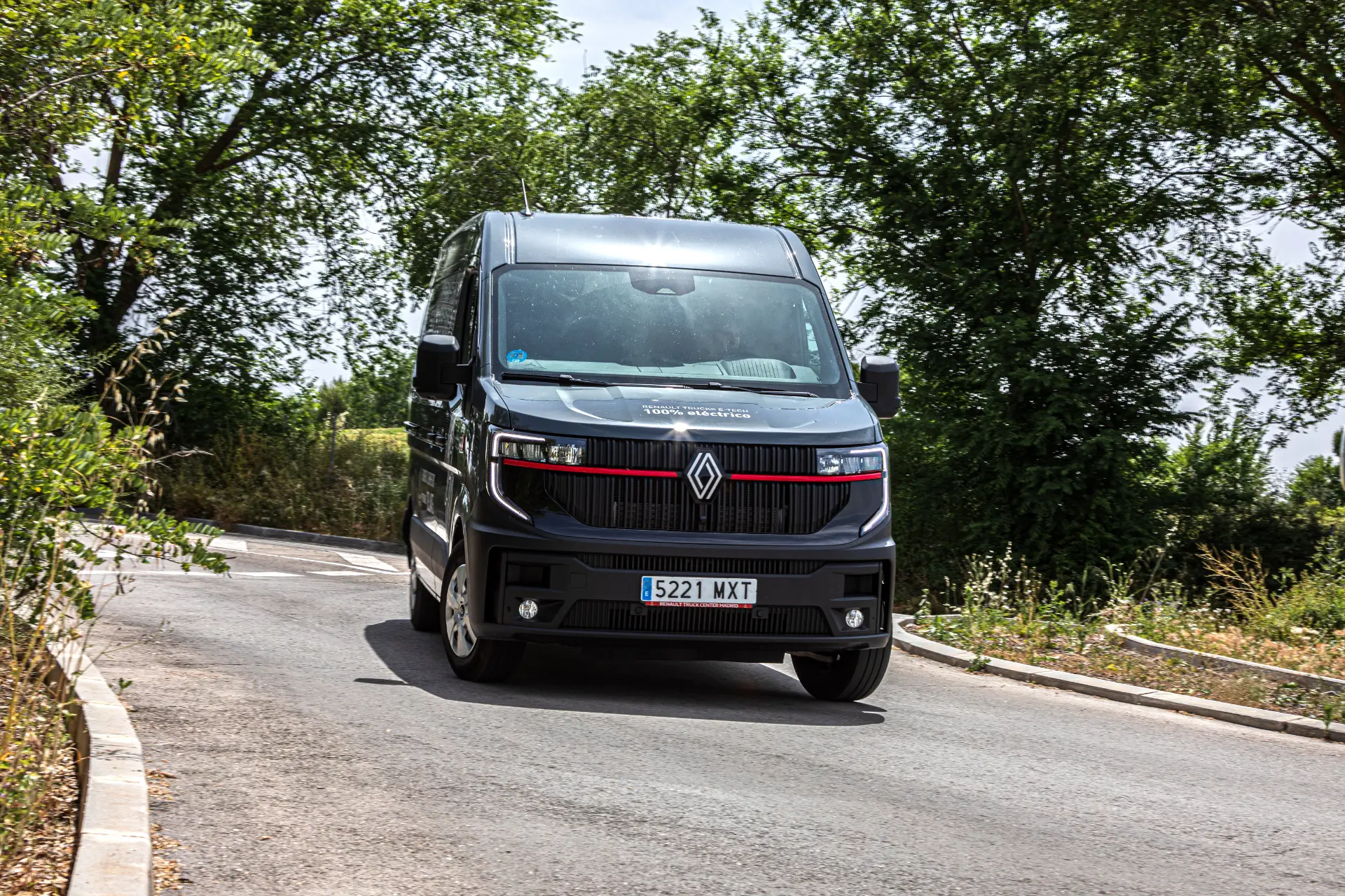 Un Renault Master furgón negro circula por una carretera de curvas rodeada de árboles y arbustos verdes.