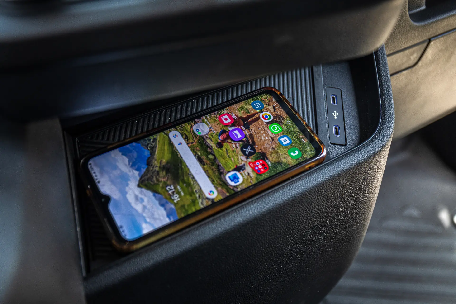 Un smartphone que se carga de forma inalámbrica en la bandeja del salpicadero de un furgón Renault, con los botones de control visibles cerca, pone de manifiesto la comodidad de las modernas furgonetas eléctricas.