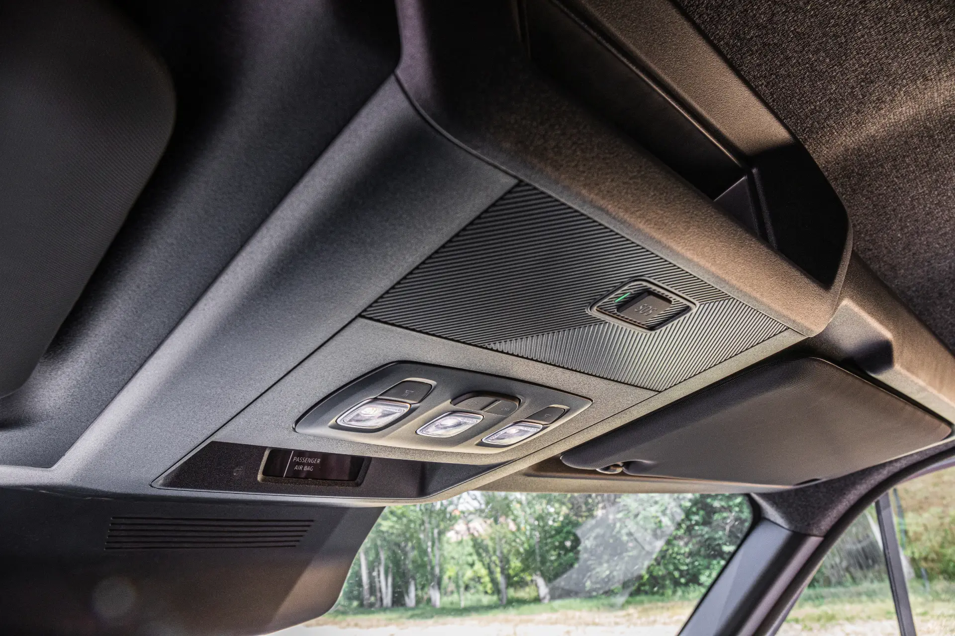 Primer plano de una consola superior de Renault Trucks Master con luces, botones y un mando para el techo solar, árboles visibles desde el exterior, características destacadas que se ven en las furgonetas eléctricas modernas.