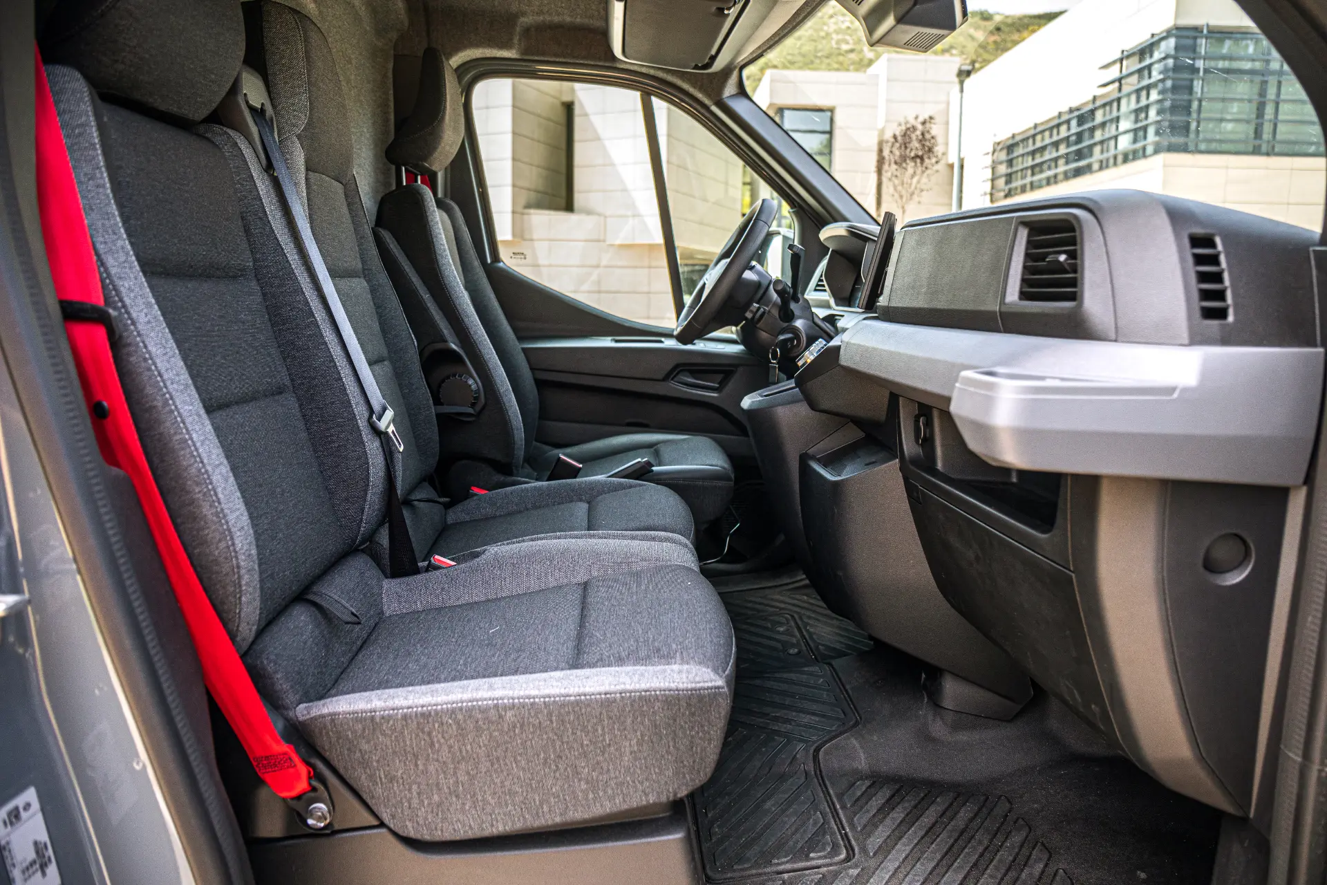 Vista interior de una furgoneta Renault Master que muestra los asientos de tela gris, el salpicadero y el volante desde el lado del pasajero: un gran ejemplo de diseño moderno de furgonetas eléctricas.