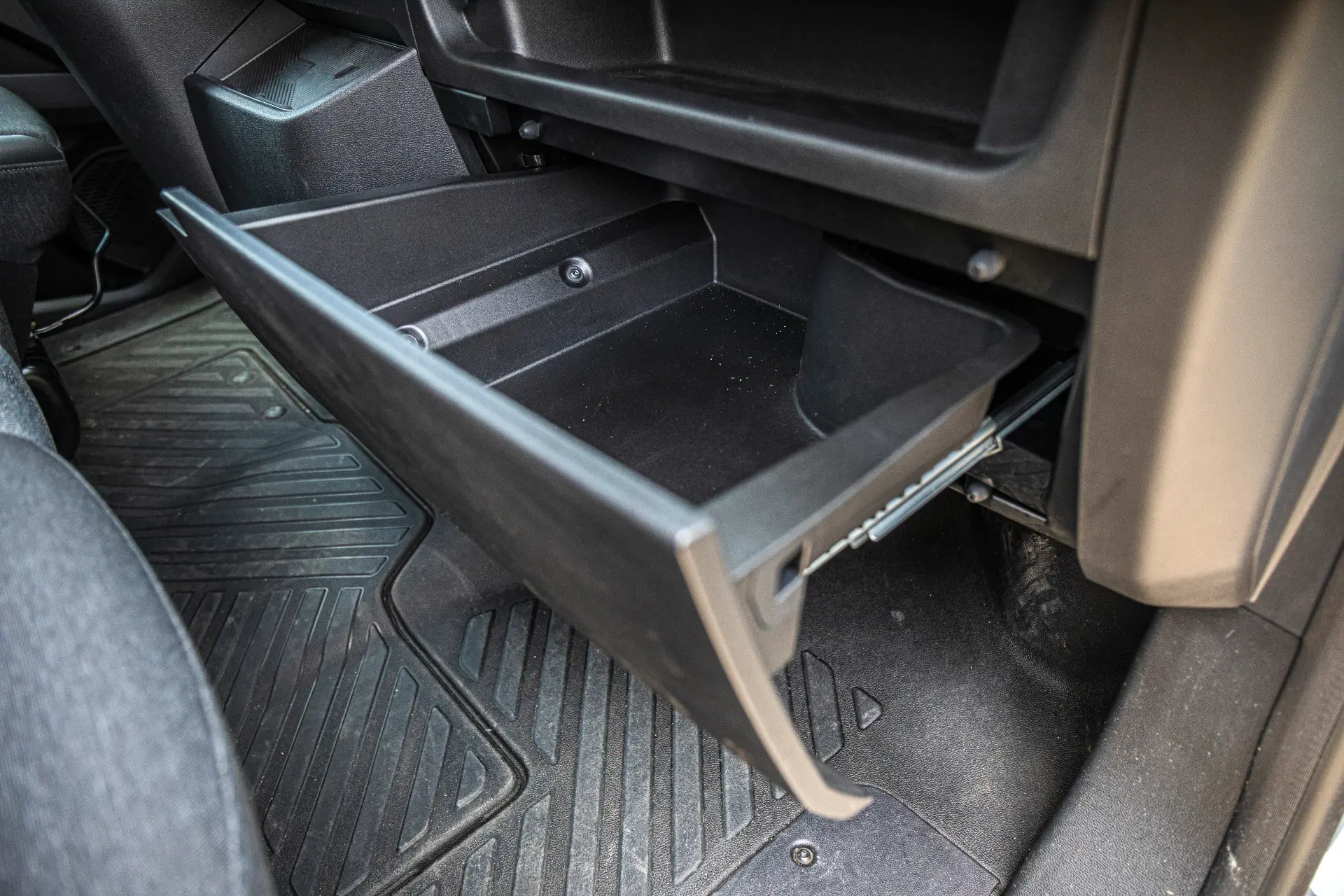 Una guantera abierta y vacía en el interior de un Renault Master con las alfombrillas negras a la vista, mostrando el práctico diseño de las furgonetas eléctricas.
