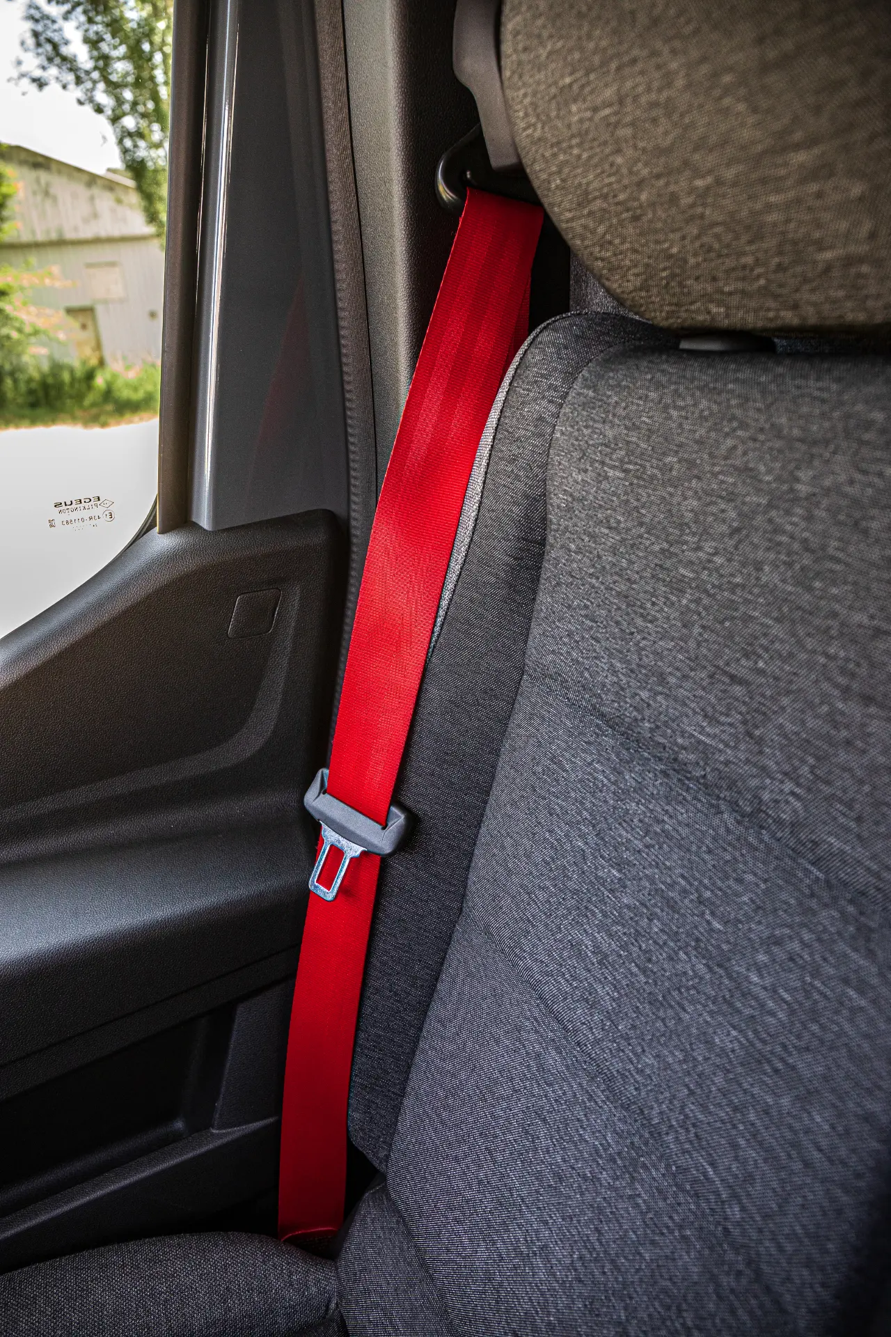 Primer plano de un asiento de coche en un furgón Renault Master, con un cinturón de seguridad rojo abrochado contra el interior de tela gris.