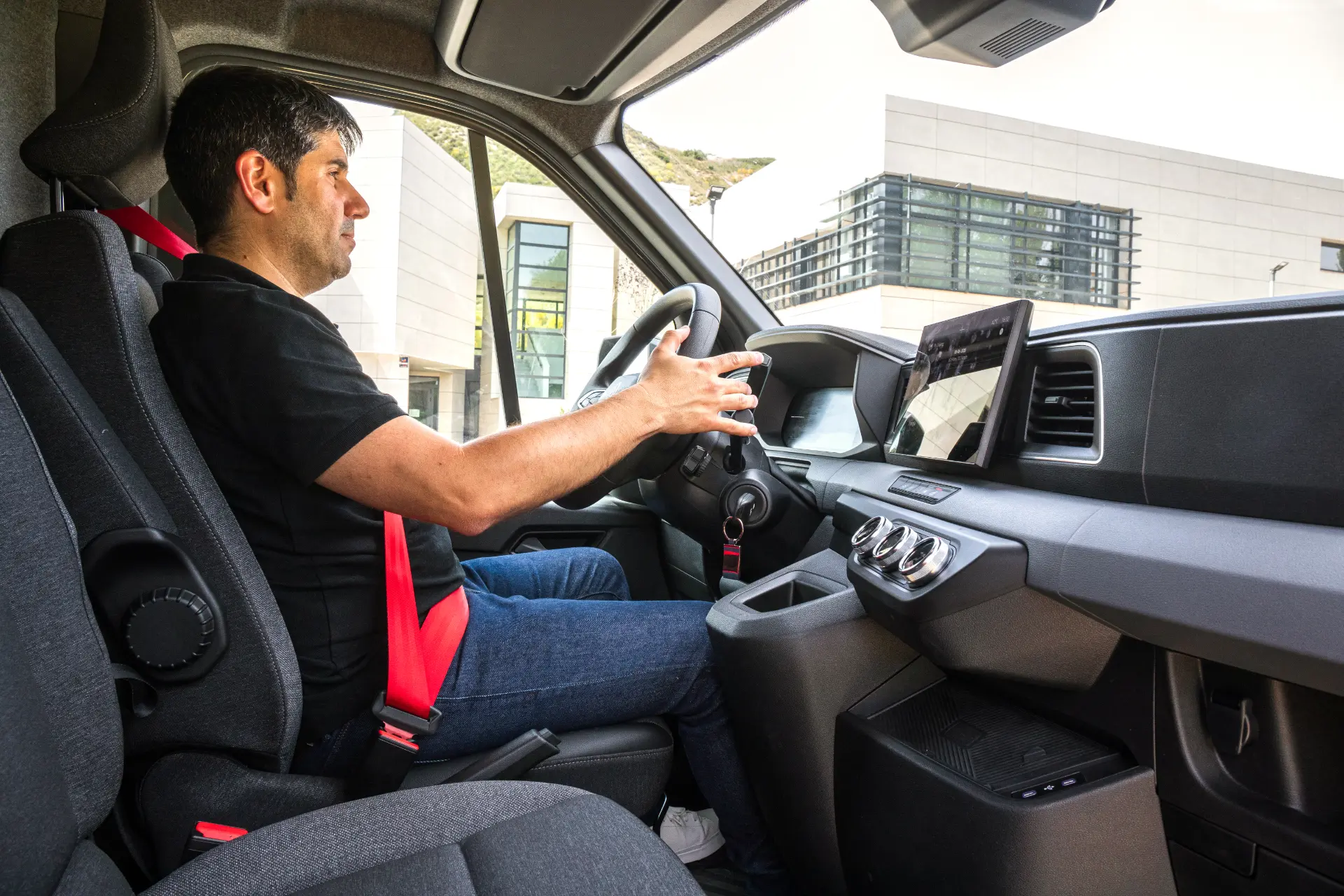 Un hombre con camisa negra se sienta en el asiento del conductor de un moderno Renault Master, sujetando con confianza el volante.