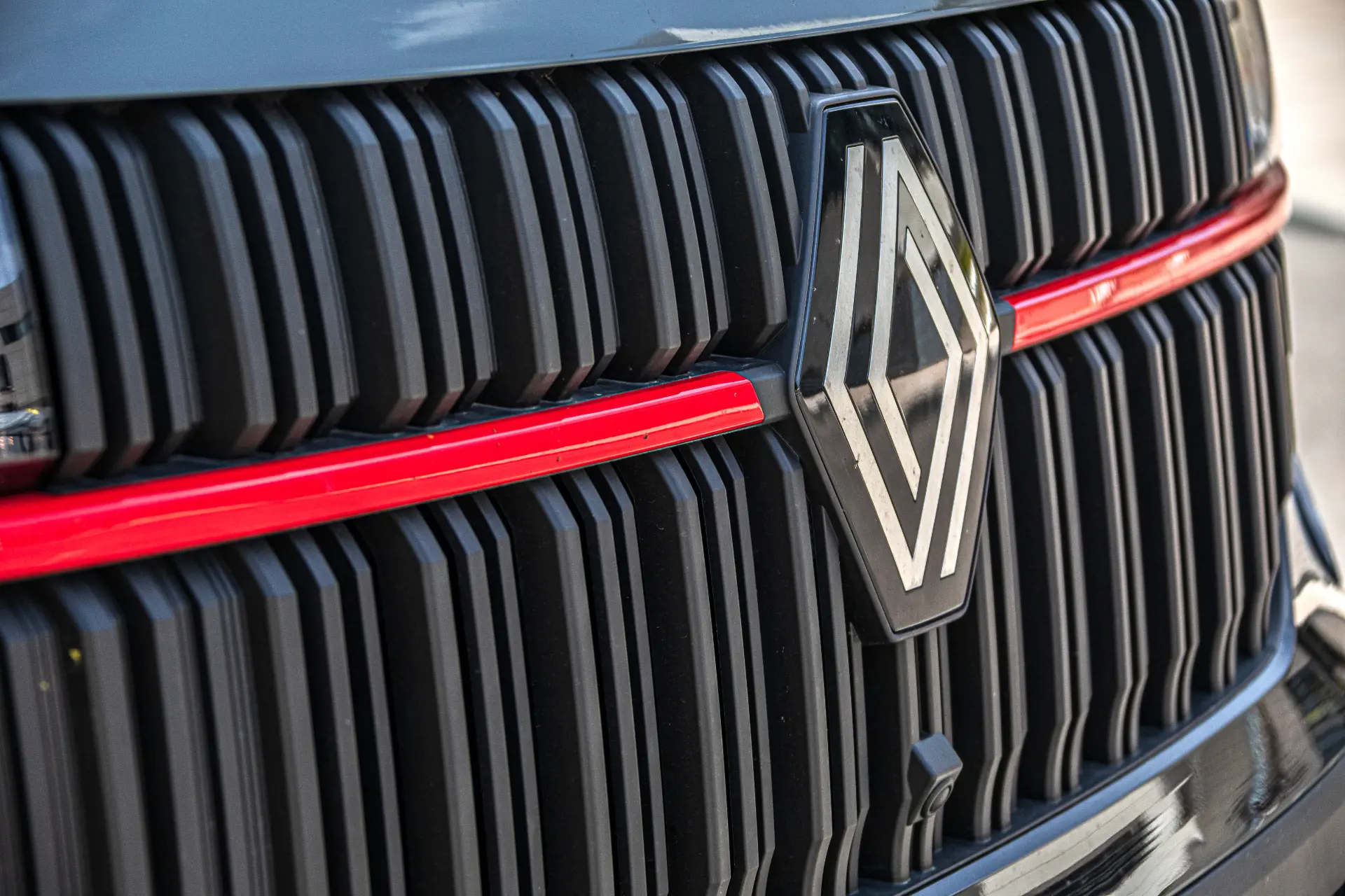 Primer plano de una calandra negra con el logotipo de Renault plateado y una línea horizontal de acento roja, que destaca el atrevido diseño visto en furgonetas eléctricas como el Renault Trucks Master y el Furgón Master.